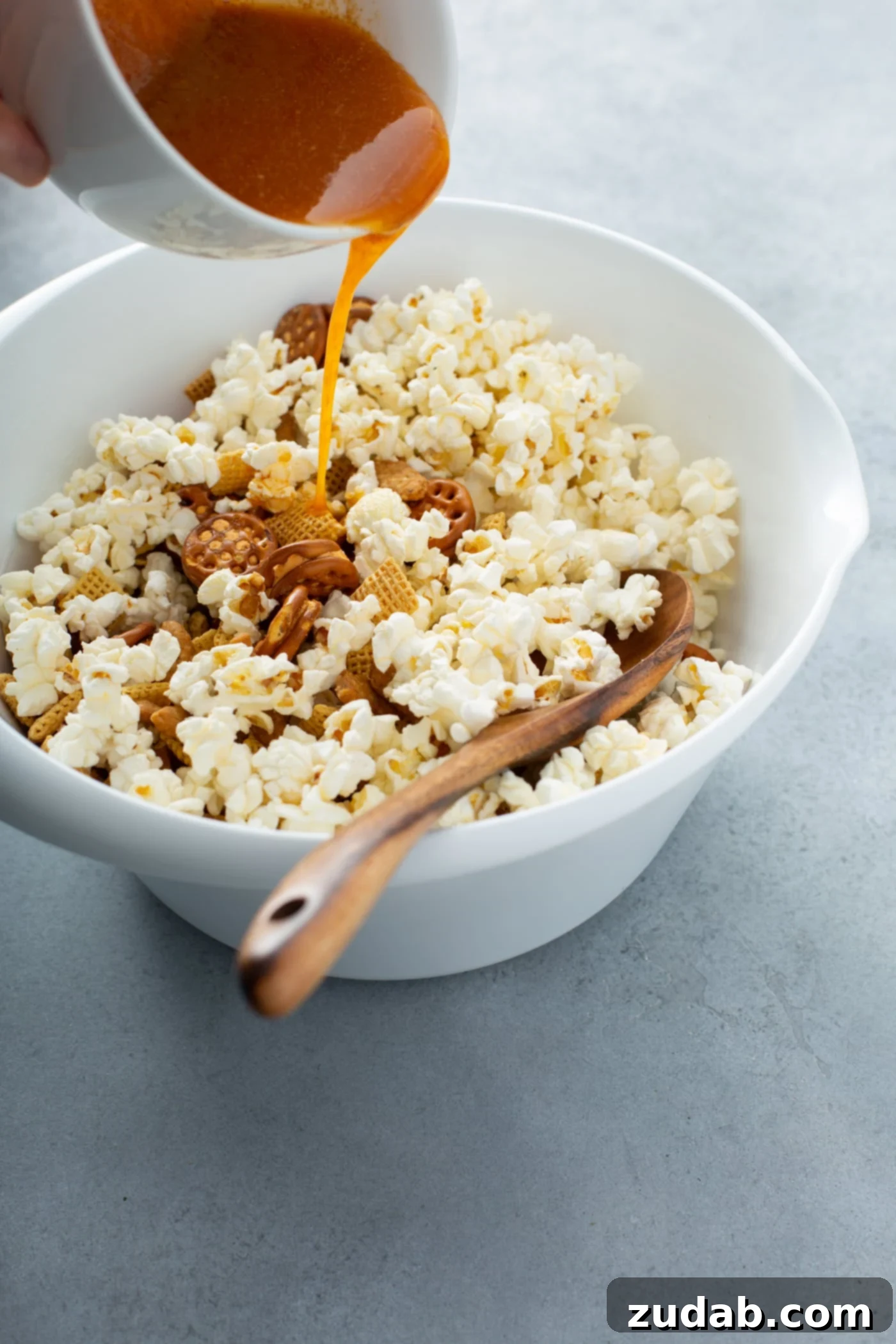 March Madness Snack Mix A bowl of popcorn other ingredients for 5 minute savory snack mix. Melted butter and spices are being poured over the popcorn.