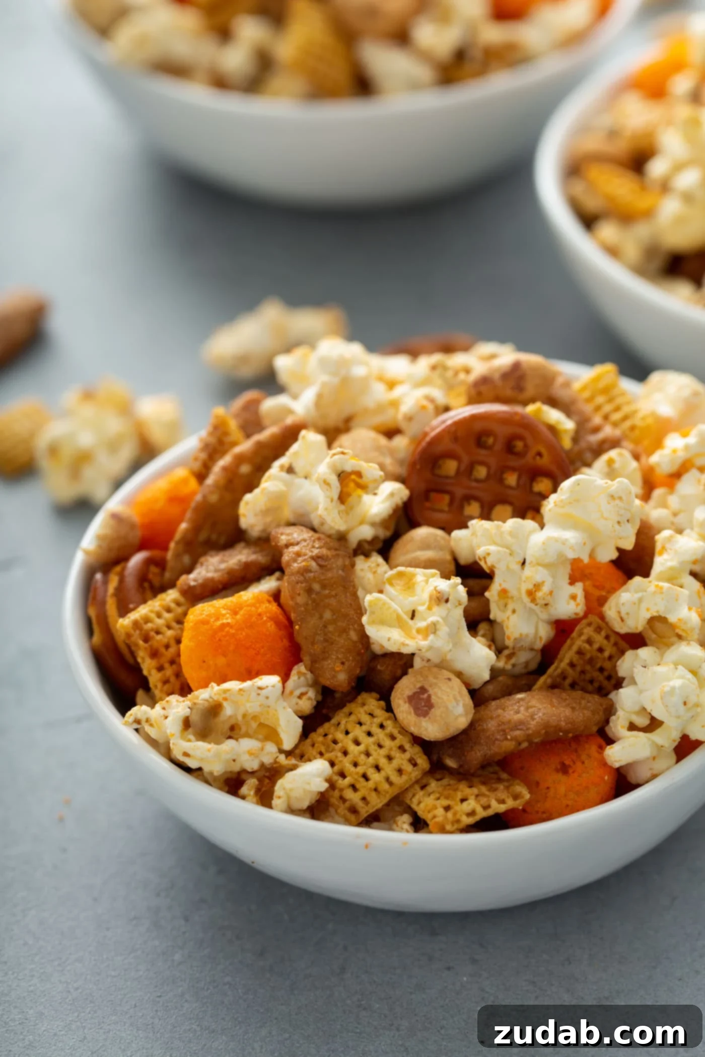 March Madness Snack Mix A bowl of savory March madness snack mix. It has popcorn, peanuts, chex, pretzels, and sesame sticks. There are other bowls of mix in the background.