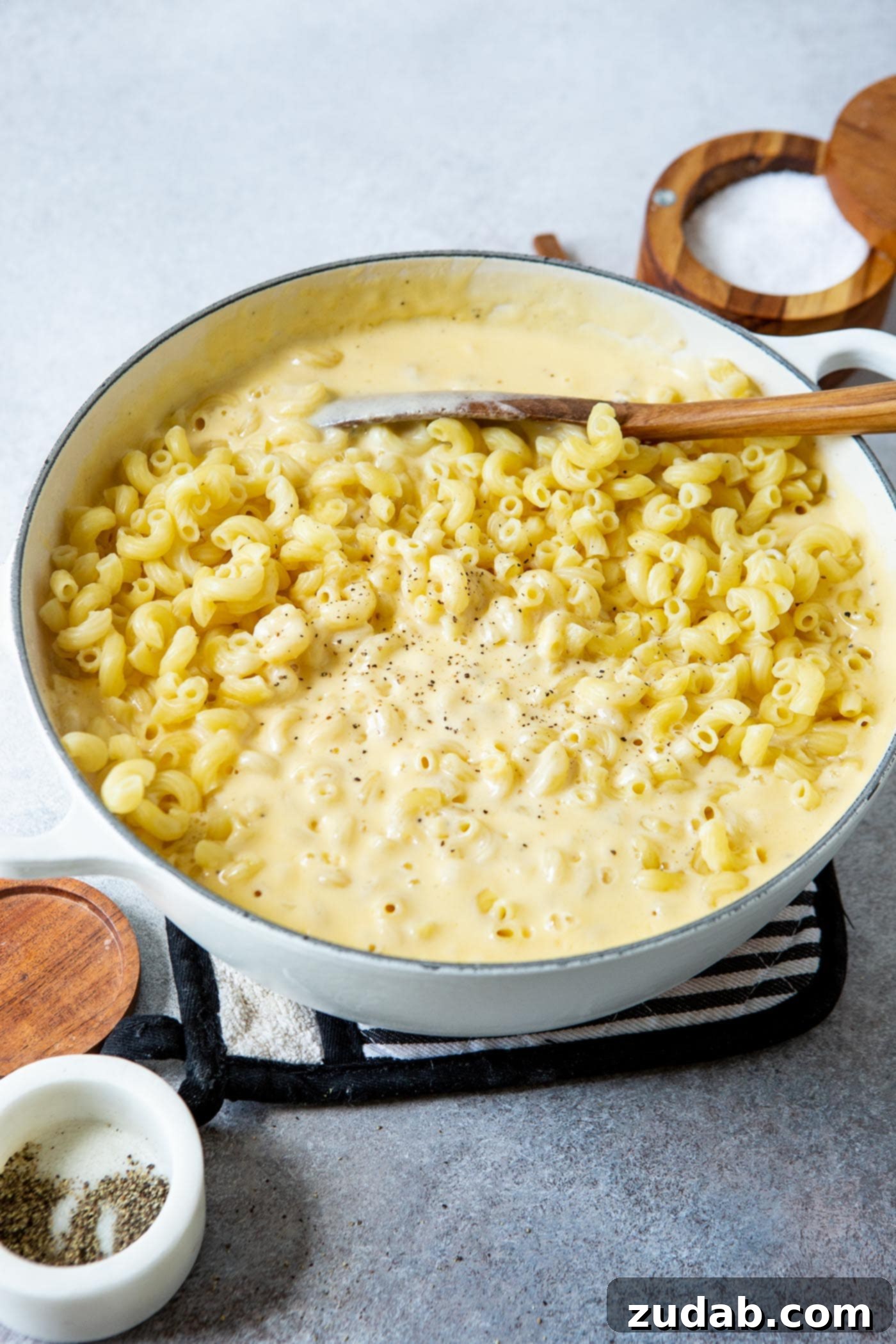 Best Macaroni and Cheese Ever A large pan filled with macaroni and a golden cheese sauce, being stirred with a wooden spoon.