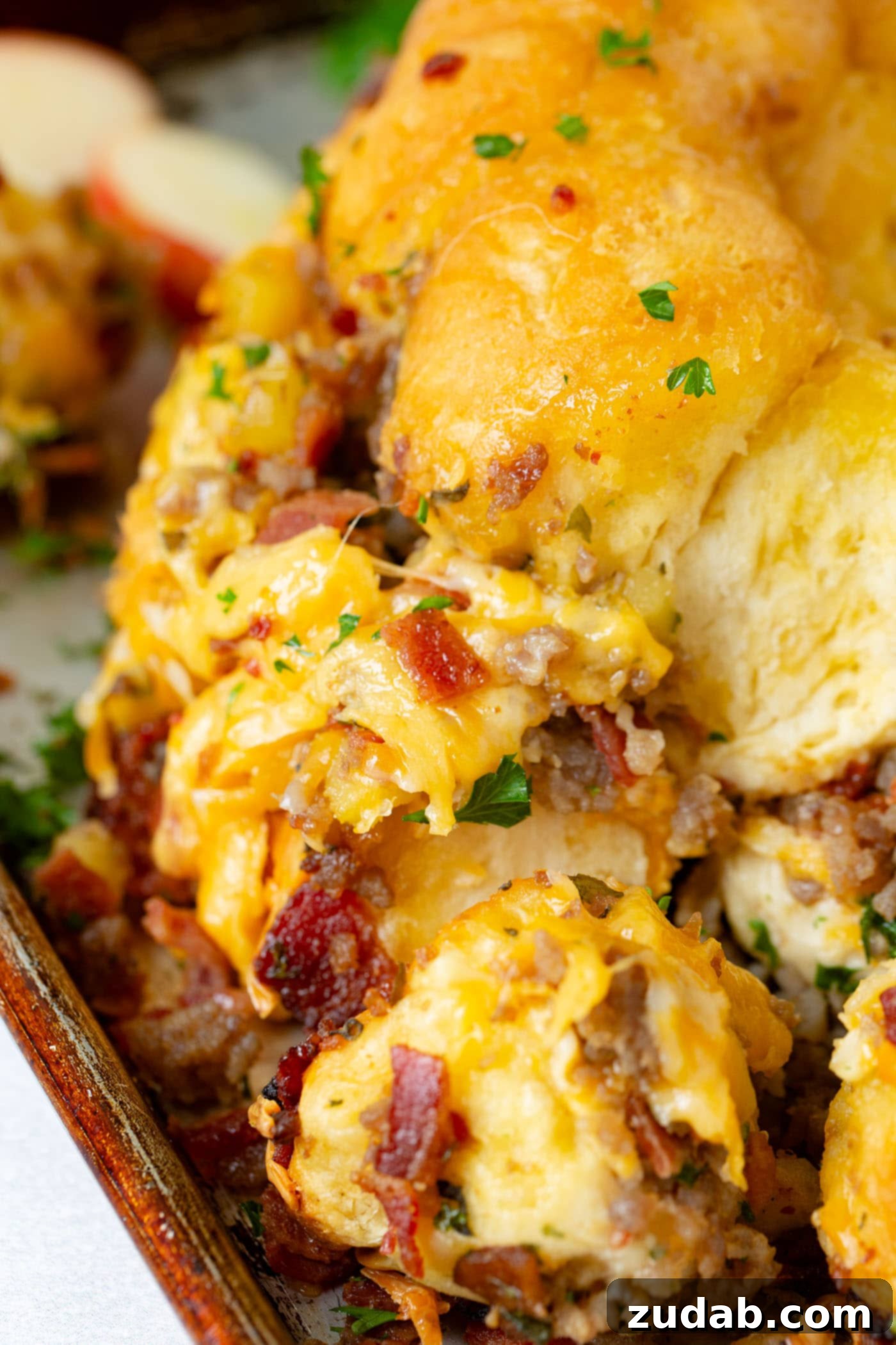 Breakfast Sausage and Apple Cheesy Pull Apart Close-up of Cheesy Pull Apart Bread, showing generous amounts of melted cheese stretching as pieces are pulled away. Bits of bacon, sausage, and bright apple chunks are visible throughout the golden-baked bread.