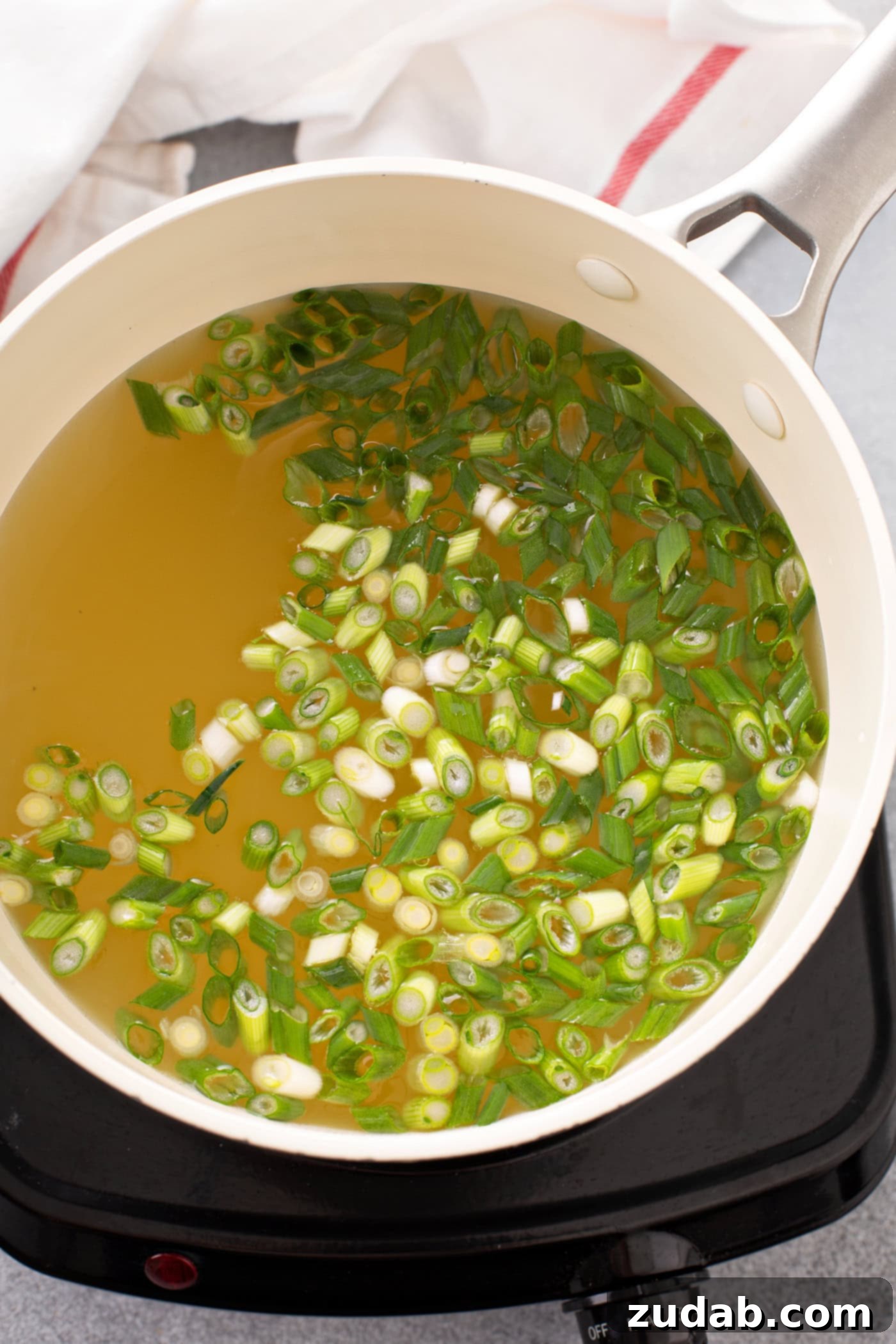 Easy Egg Drop Soup A bowl containing chicken broth and slices green onions.