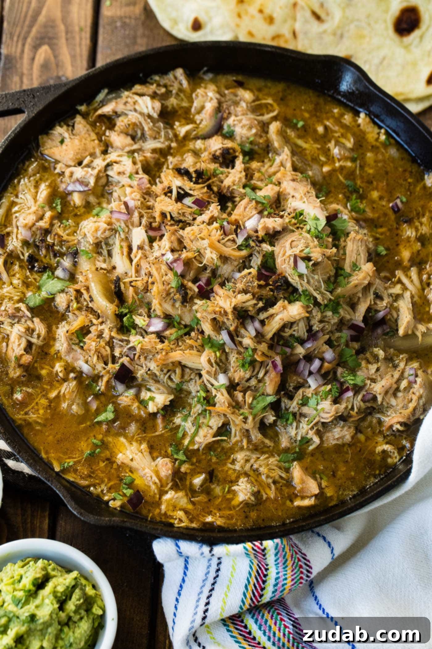 Slow Cooker Chicken Carnitas A photo of juicy crispy chicken carnitas in a cast iron skillet garnished with chopped cilantro and diced red onion.