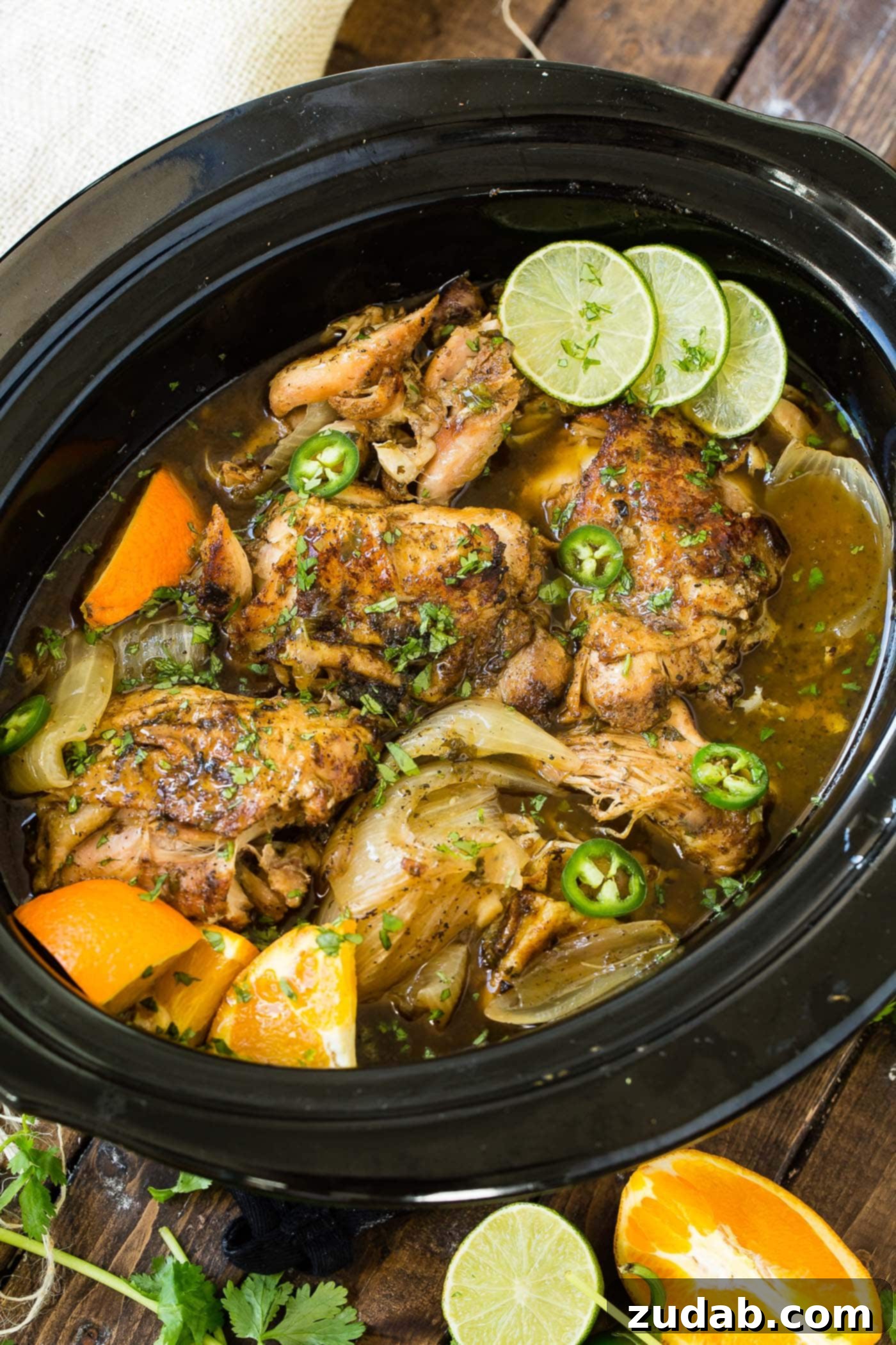 Slow Cooker Chicken Carnitas A photo of chicken carnitas being cooked in a slow cooker witl slices of fresh lime.