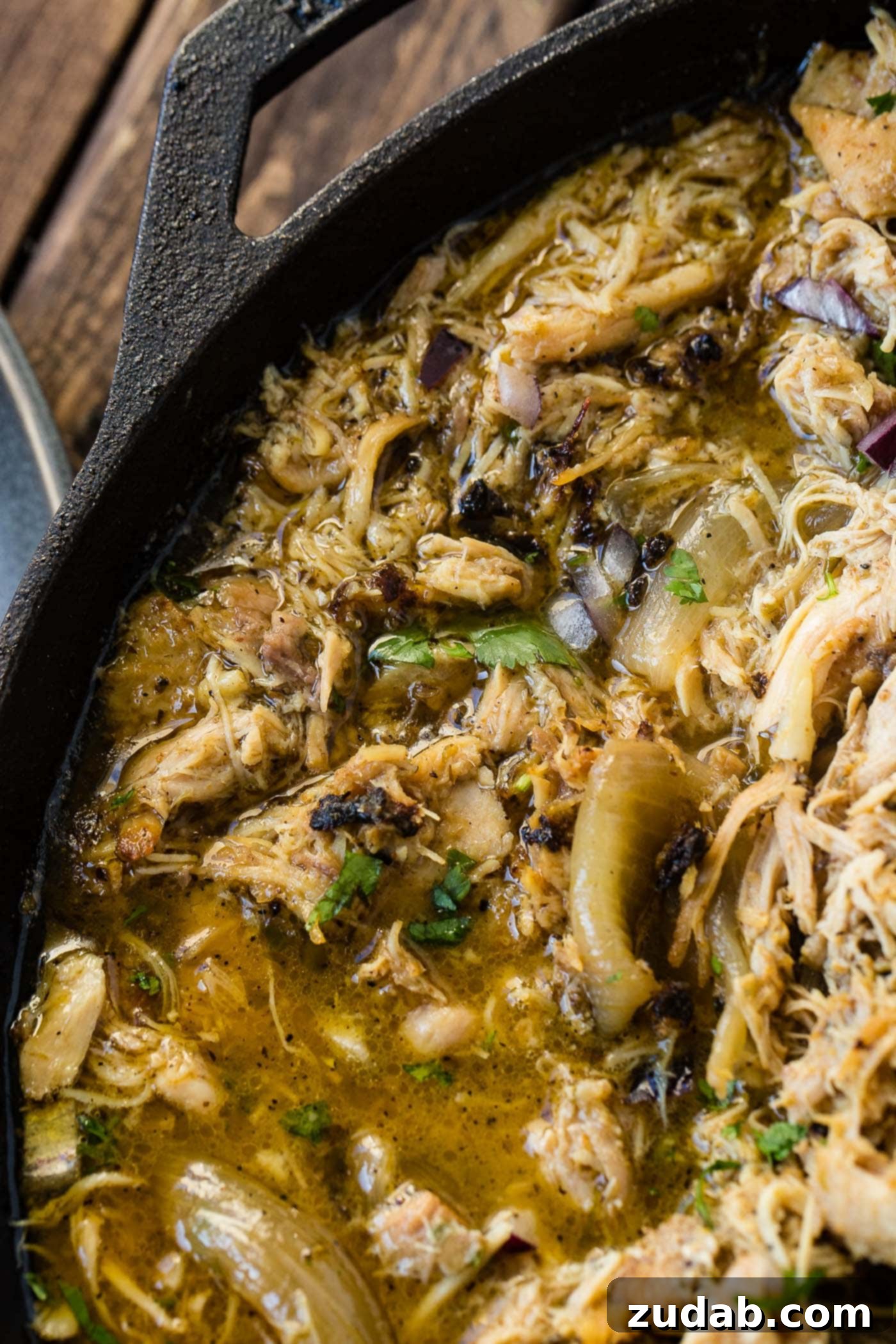 Slow Cooker Chicken Carnitas A photo of juicy crispy chicken carnitas in a cast iron skillet garnished with chopped cilantro and diced red onion.