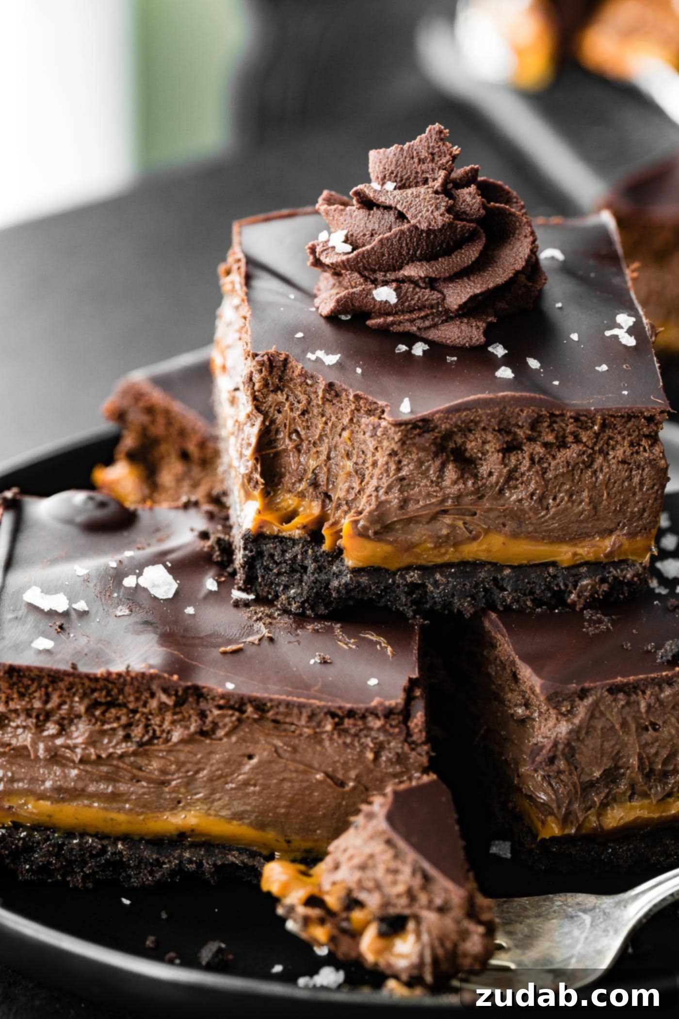 Decadent Dulce de Leche Chocolate Cheesecake Squares 7 a bite is taken out of a layered Dulce de Leche Dessert Cream Cheese Bar with whipped ganache on top. The dessert is layered with oreo crust, creamy caramel, chocolate cheesecake filling, and a chocolate ganache topping.
