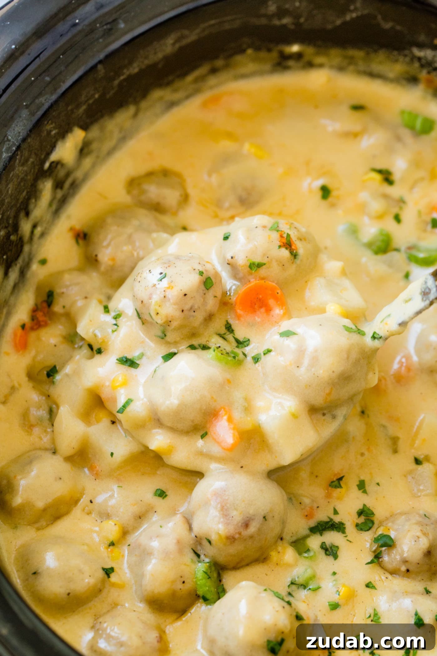 Close-up of a slow cooker filled with bubbling, creamy cheesy meatball soup, showcasing chunks of potatoes, carrots, and meatballs.