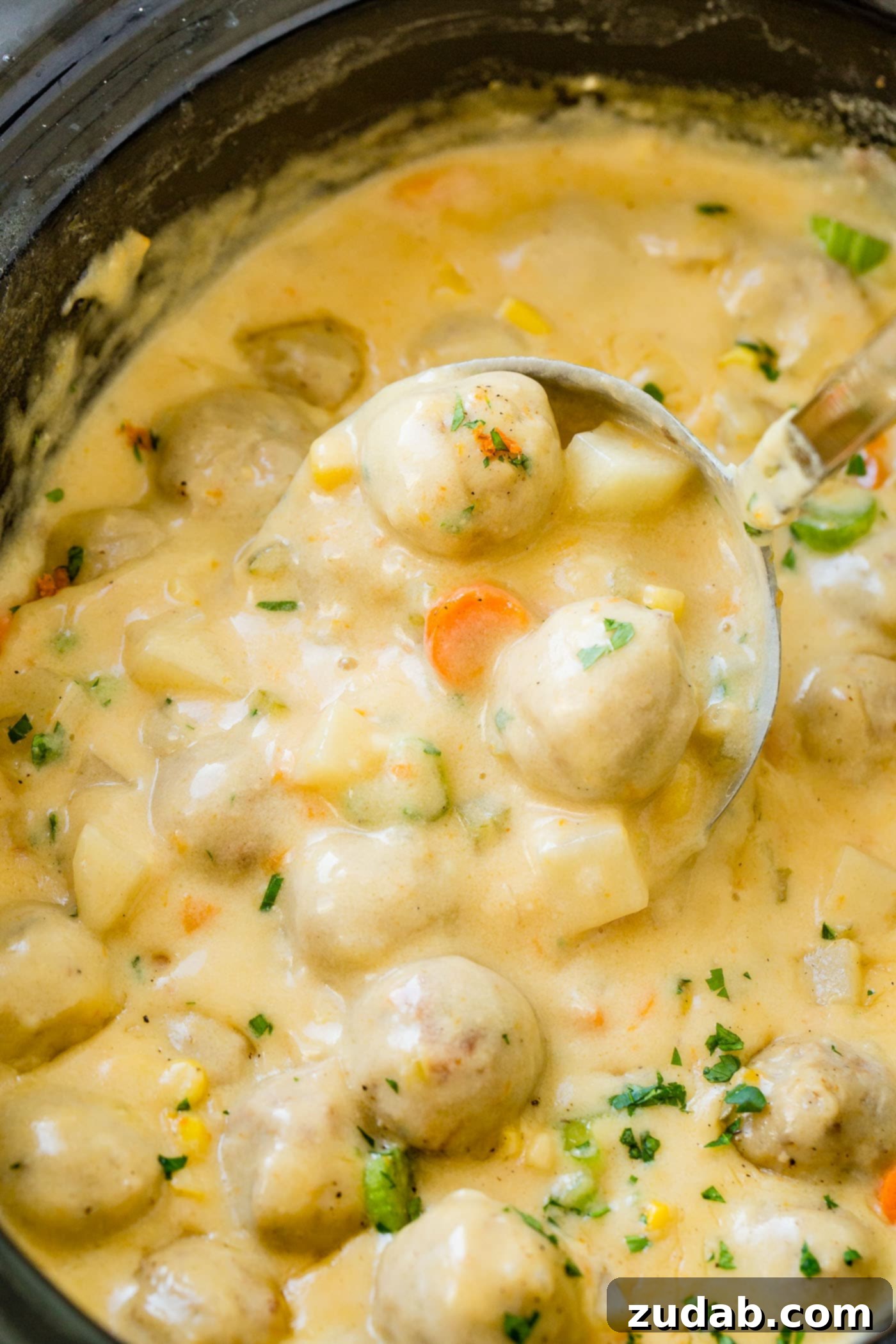 An overhead view of a slow cooker filled to the brim with creamy, cheesy meatball soup, garnished with fresh herbs and ready to be served.