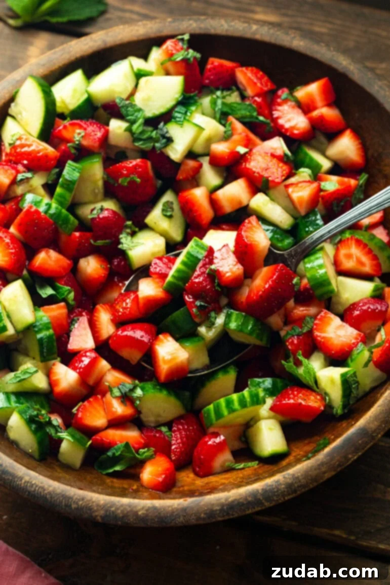 Vibrant Strawberry Cucumber Salad with Honey Balsamic 3 a photo of a wooden serving bowl full of cucumber strawberry salad being stirred with a large metal spoon.