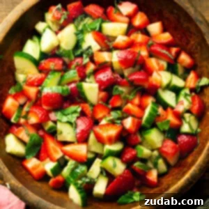 a photo of a wooden serving bowl full of strawberry cucumber salad