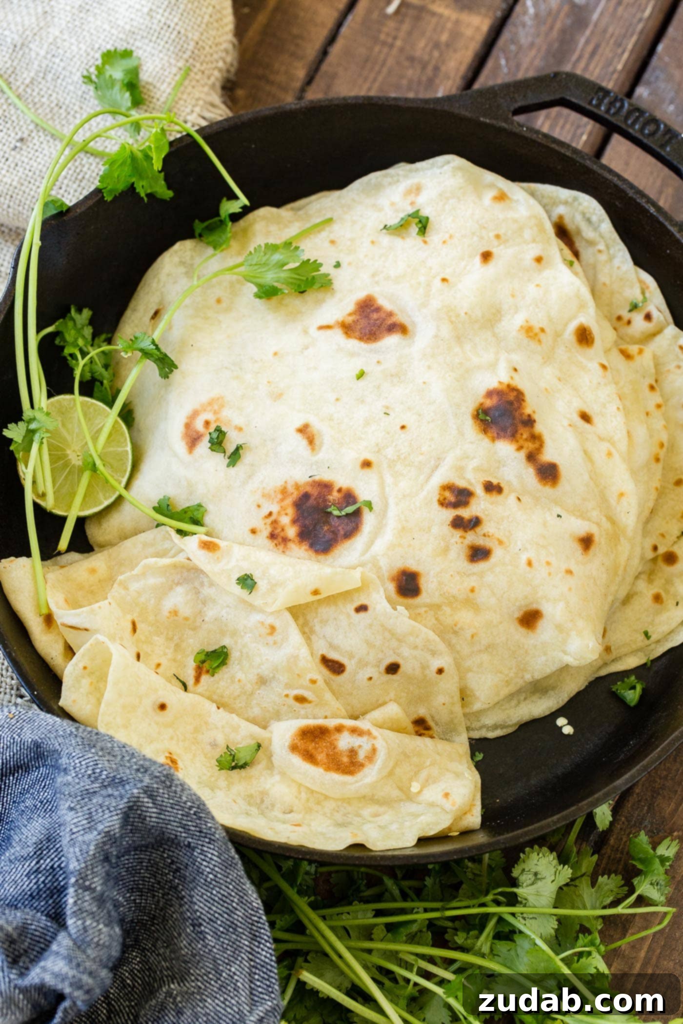 A photo of a stack of cooked homemade flour tortillas in a cast iron skillet.