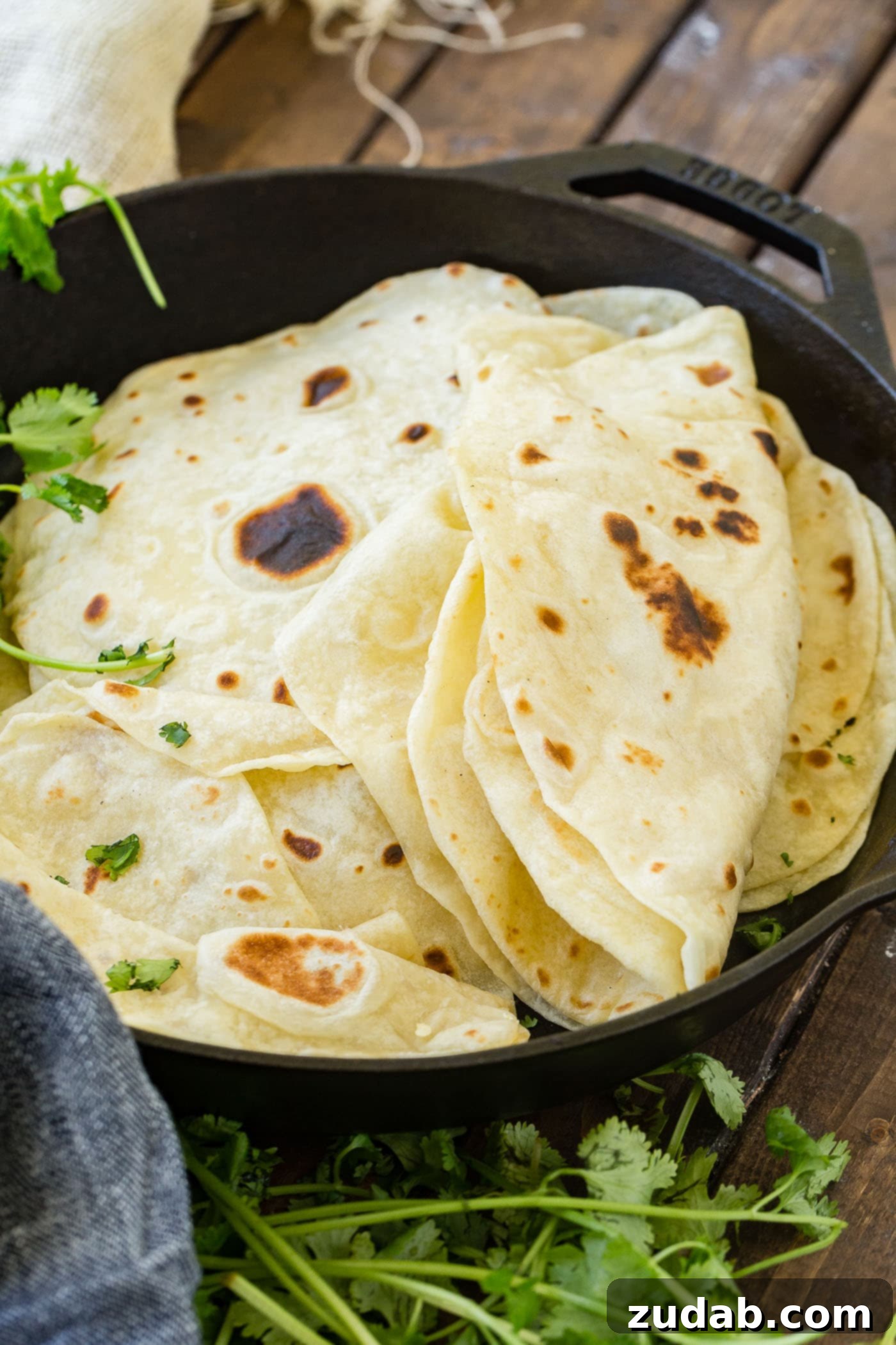 A photo of a stack of cooked homemade flour tortillas in a cast iron skillet with the top few tortillas folded in half.