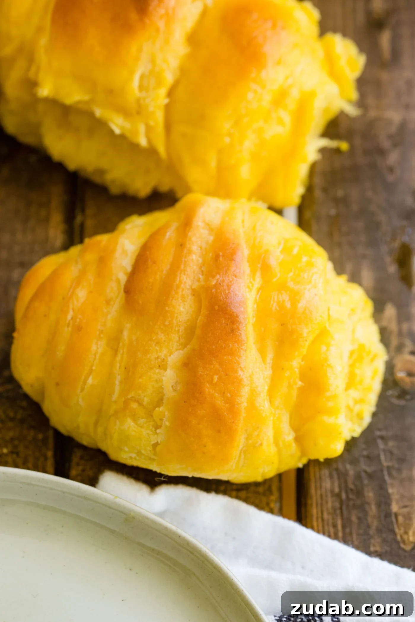 Pillowy Pumpkin Dinner Rolls 6 A fresh pumpkin dinner roll served on a rustic wood table, highlighting its golden crust and inviting texture