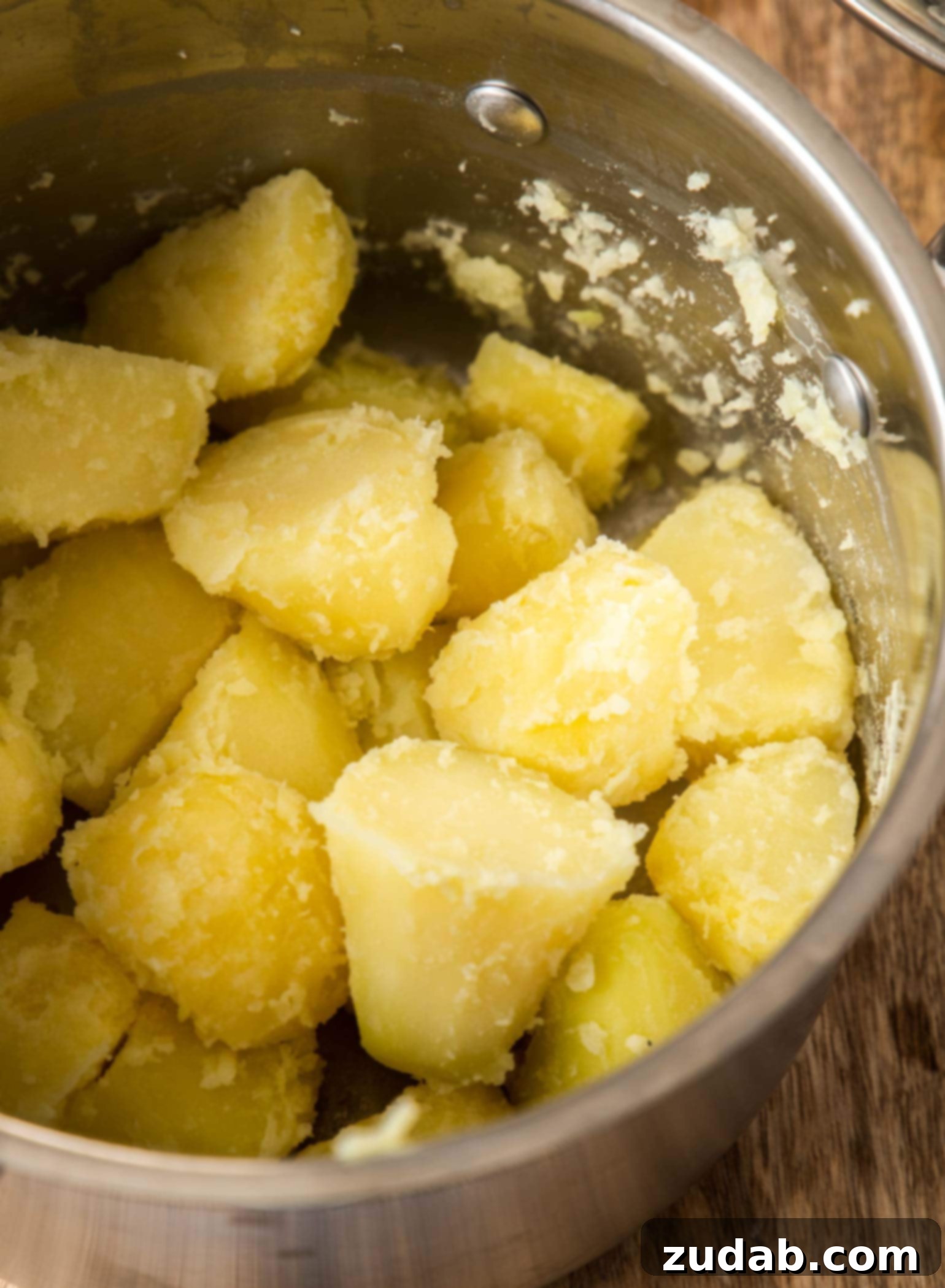 Crispy Garlic-Herb Roasted Potatoes 4 A close-up view of a saucepan filled with par-boiled Yukon Gold potatoes. The potatoes appear slightly roughed up, with broken edges, indicating they've been prepared for roasting to achieve maximum crispiness.