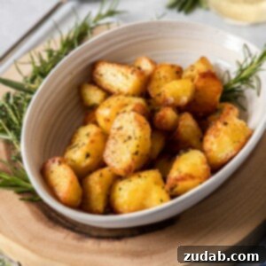 Crispy Garlic-Herb Roasted Potatoes 8 A cream coloured bowl filled with herby roasted potatoes, surrounded by fresh herbs. It sits on a wooden board