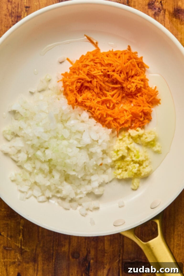 Our Favorite Classic Meatloaf 5 Close-up of minced garlic, chopped onions, and shredded carrots sautéing in a hot skillet with vegetable oil, preparing the aromatic base for the meatloaf.