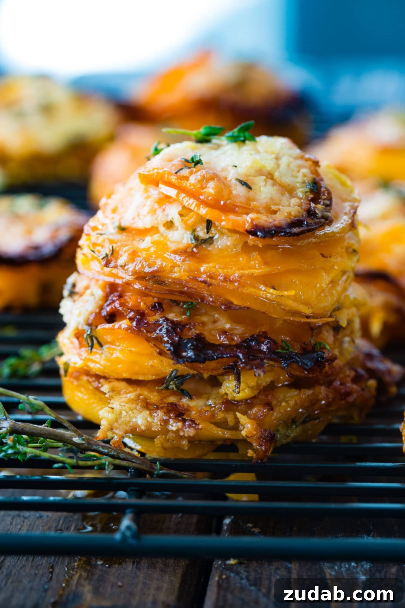 Cheesy Gruyere Sweet Potato Stacks A photo of a stack of thinly sliced sweet potatoes layered with gruyere and parmesan cheese and topped with fresh thyme, presented beautifully.