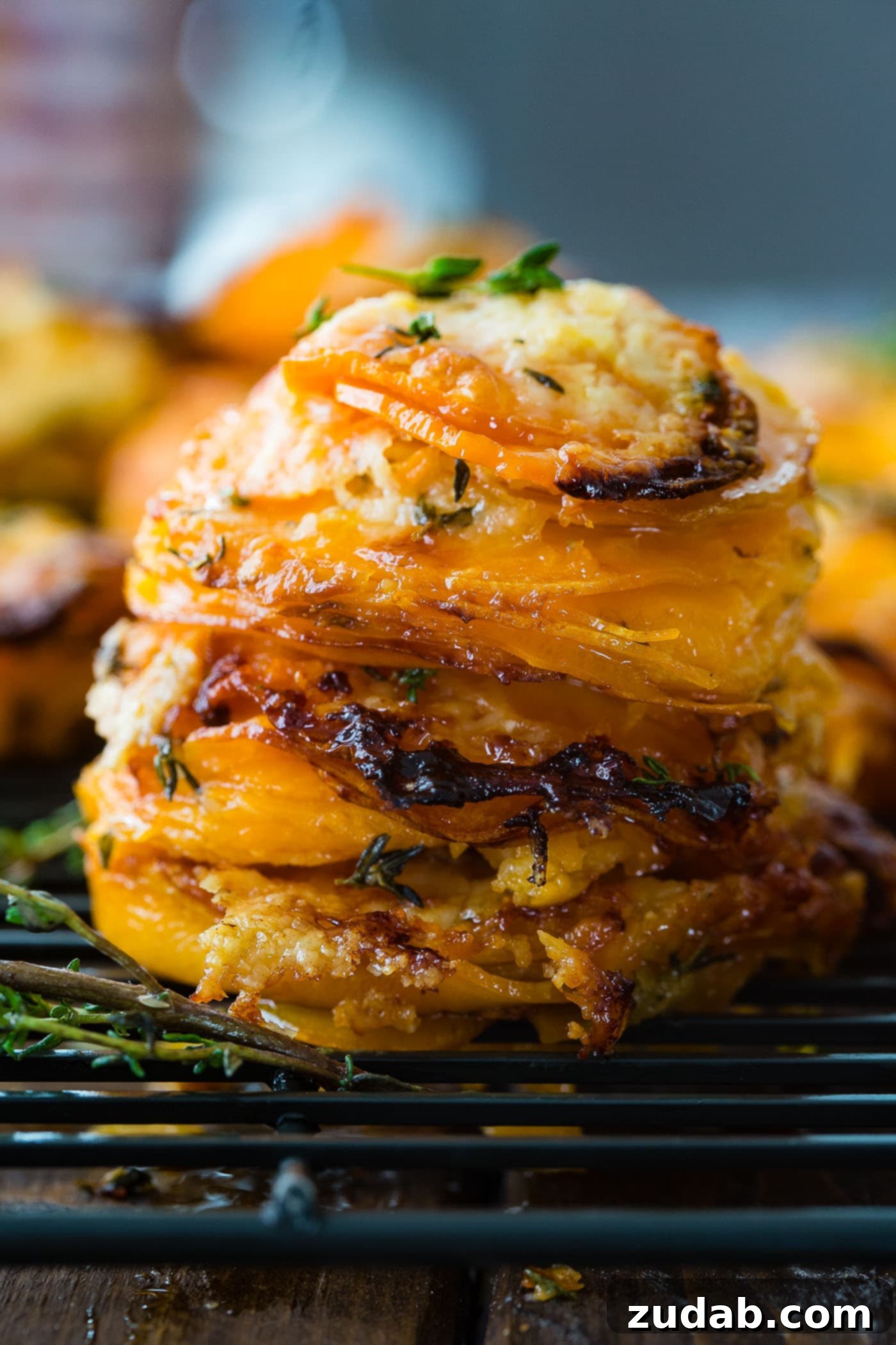 Cheesy Gruyere Sweet Potato Stacks A stunning sweet potato stack, golden and cheesy, garnished with fresh thyme, presented beautifully on a clean surface.