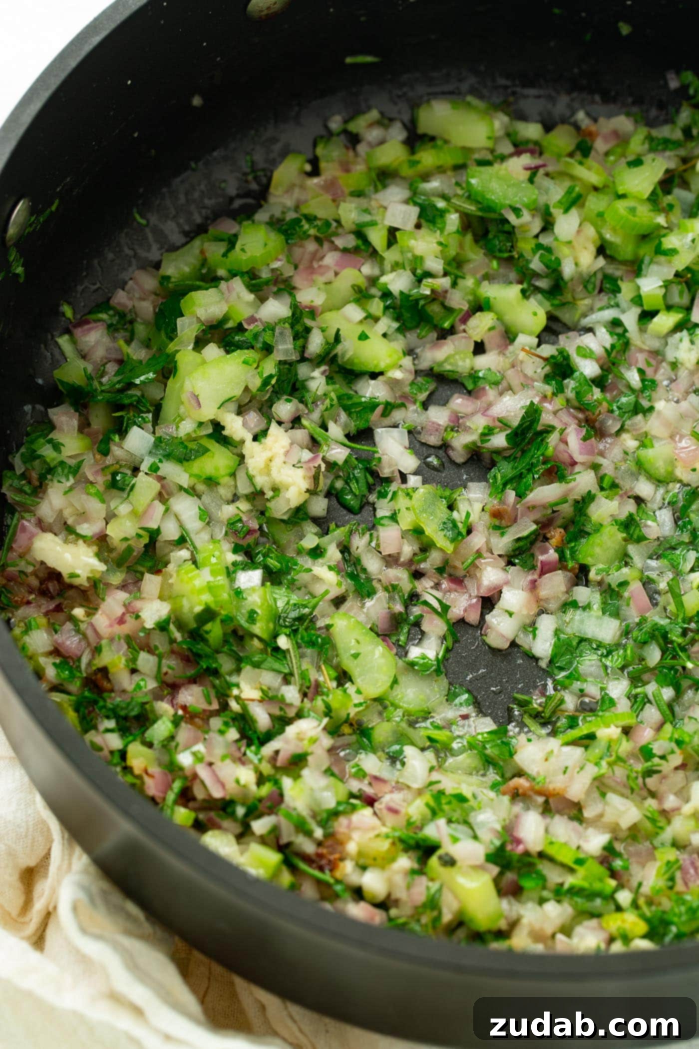 Make Ahead No Fuss Stuffing A photo of sauteed shallots, celery, garlic and fresh herbs in a skillet.