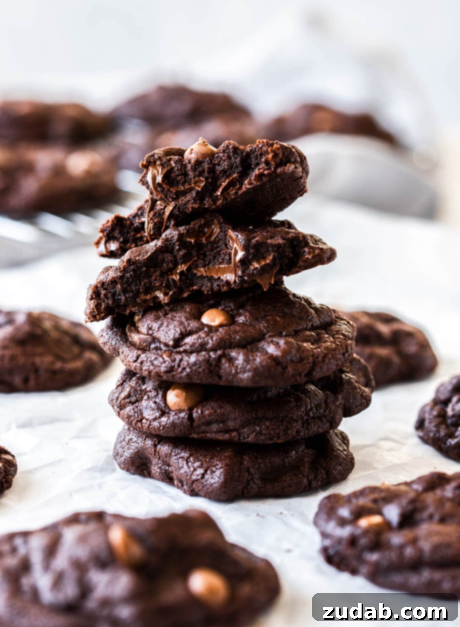 Signature Bakery Chocolate Cookies 5 A chocolate cookie broken in half sitting on top of a stack of cookies, showing the gooey chocolate chip centre