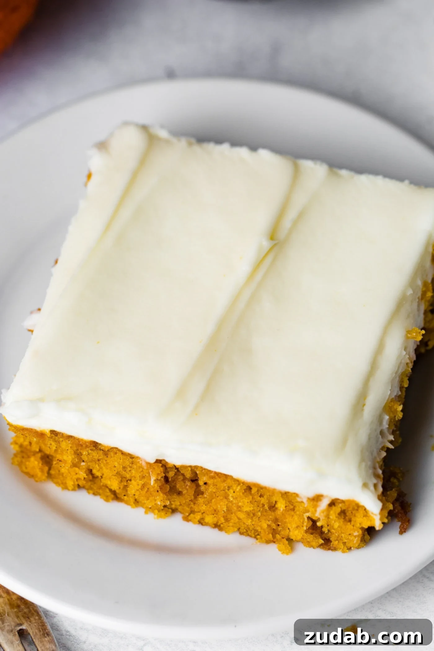 Pumpkin Sheet Cake A photo of a piece of pumpkin sheet cake with cream cheese frosting sitting on a white plate.