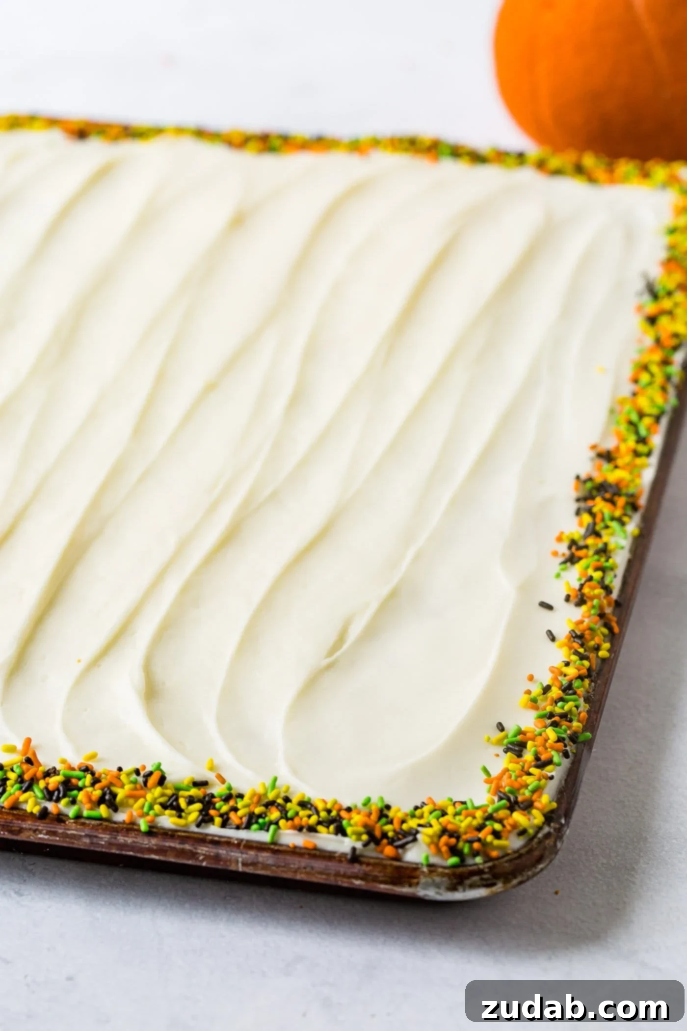 Spiced Pumpkin Sheet Cake 2 A photo of a whole pumpkin sheet cake that is frosted with cream cheese frosting and lined around the edges with fall sprinkles.