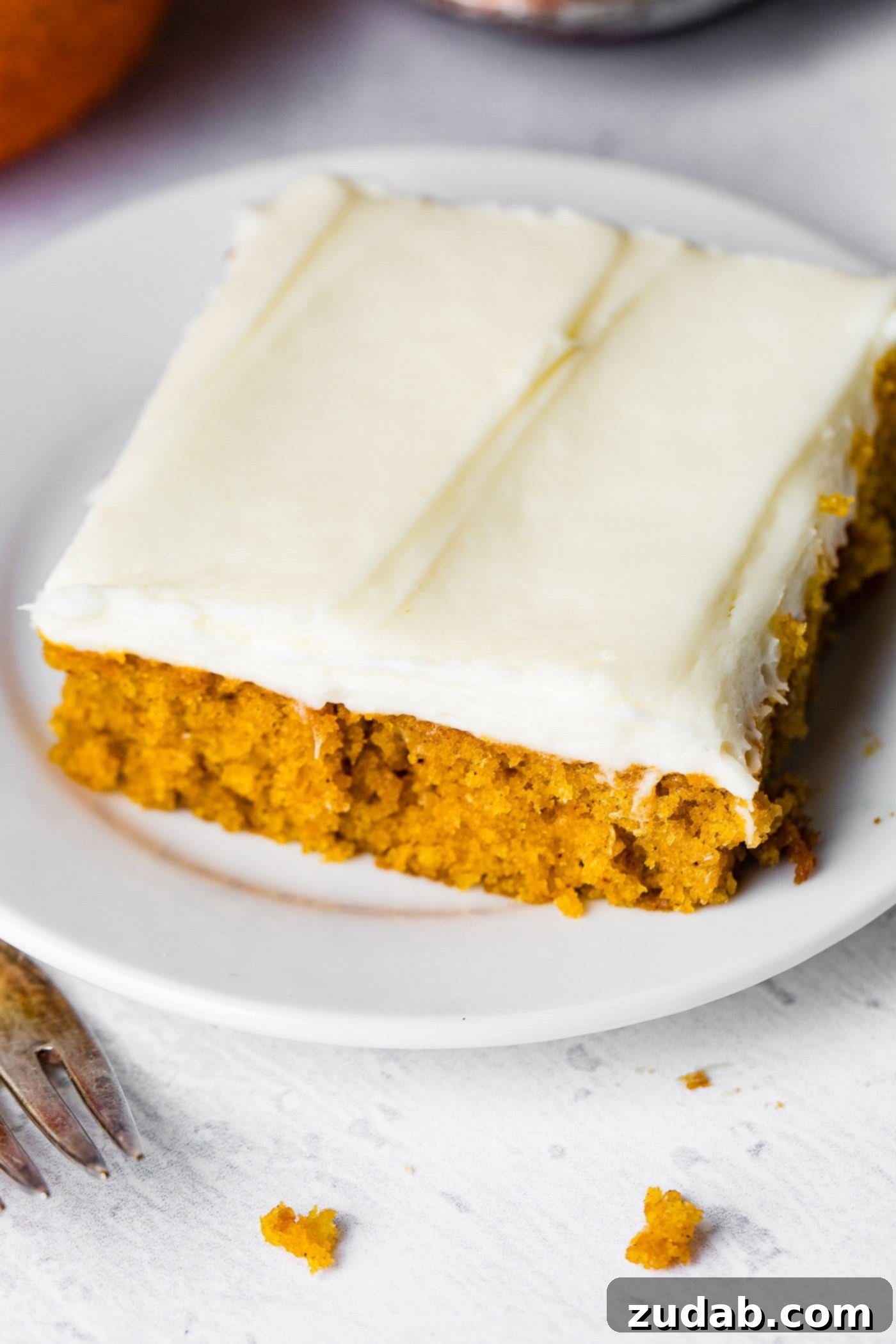 Pumpkin Sheet Cake A photo of a piece of pumpkin sheet cake with cream cheese frosting sitting on a white plate.