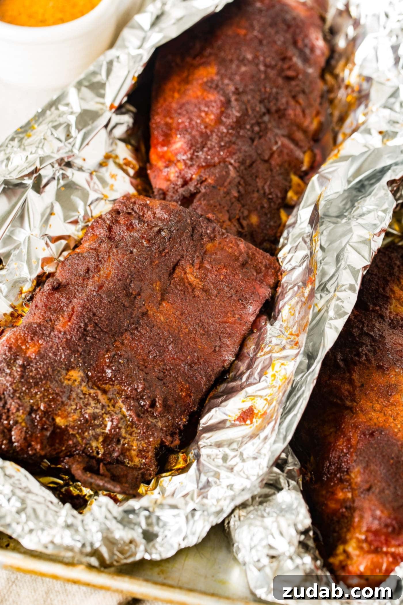A photo of smoked ribs hot off the smoker still wrapped in foil with the foil just opened on the top, revealing the succulent meat.