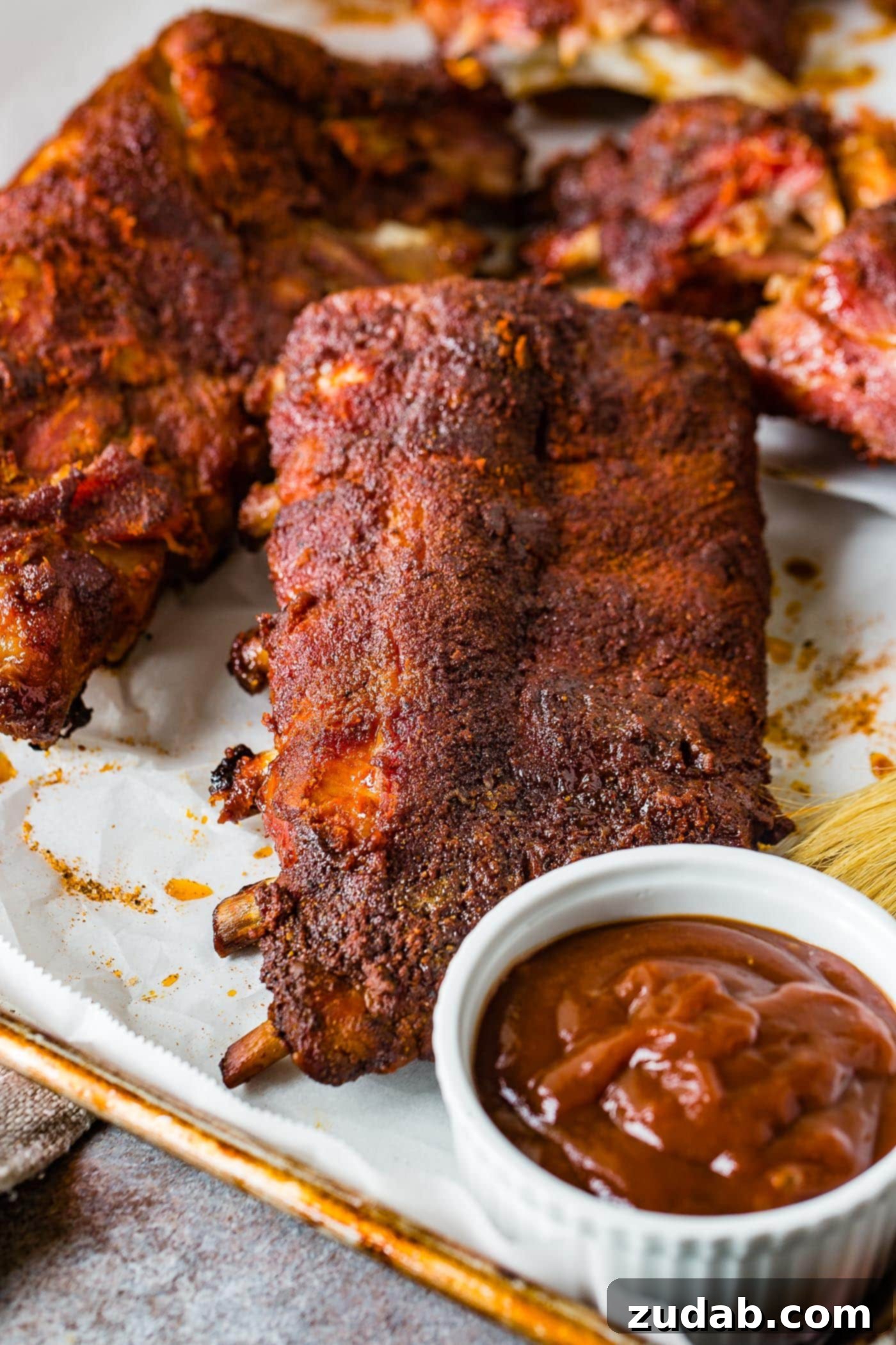 A photo of a rack of smoked ribs with a cup of BBQ sauce next to it, invitingly presented.