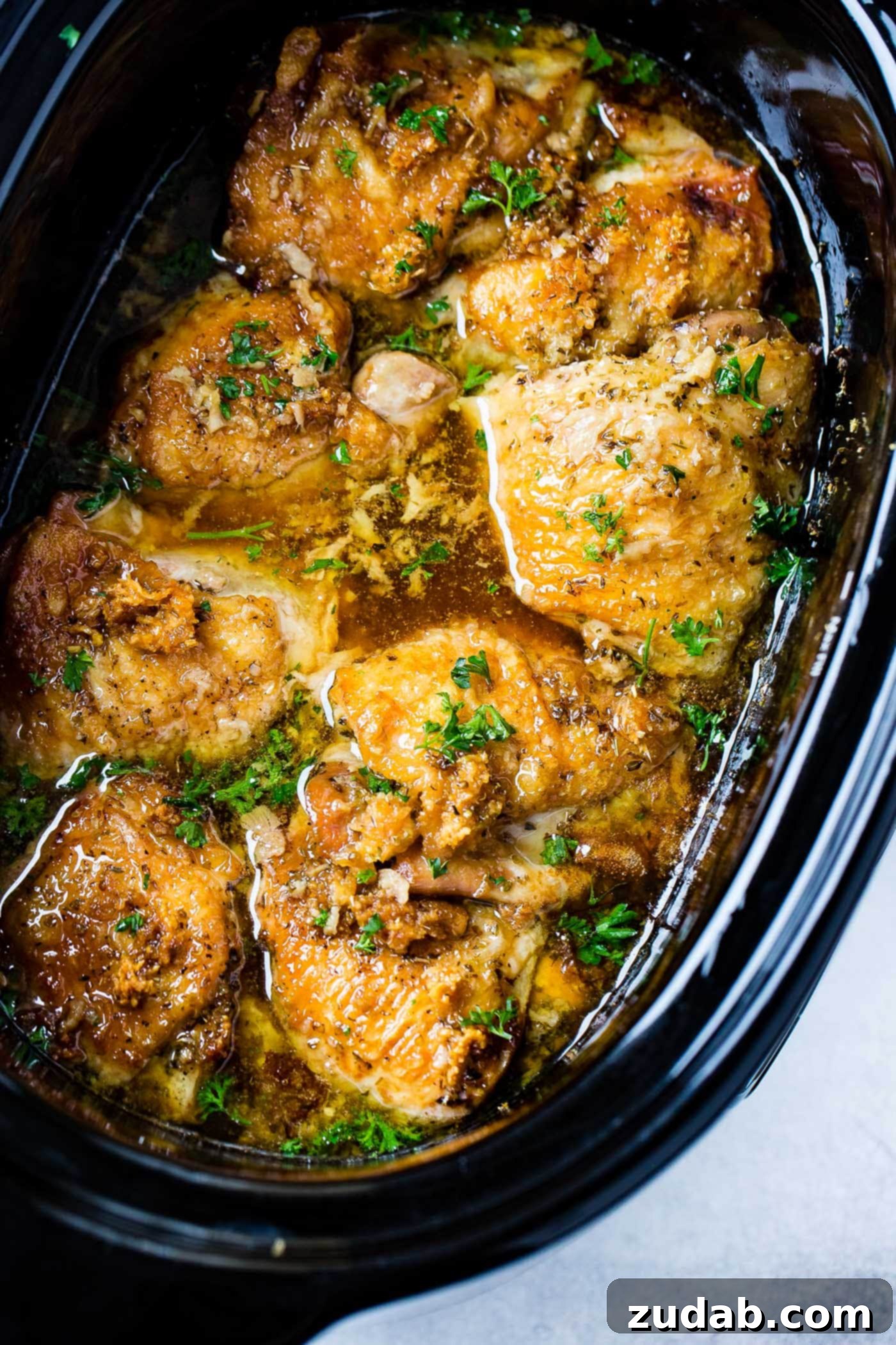 A close-up photo of Slow Cooker Garlic Chicken in a crock pot, garnished with fresh chopped parsley, highlighting its rustic appeal.