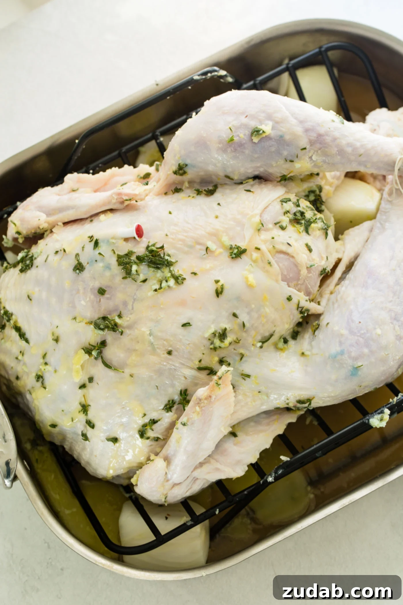 The Best Oven Roasted Thanksgiving Turkey Ever A photo of an uncooked whole turkey lathered in herb butter sitting in a roasting pan.