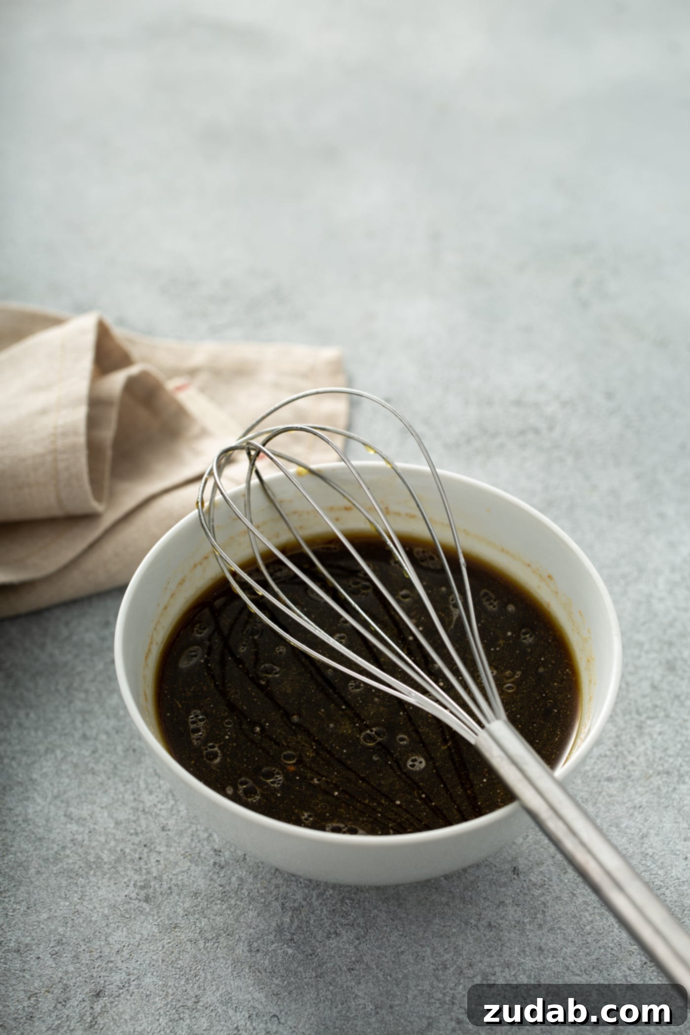 Instant Pot Beef and Broccoli A photo of the sauce for beef and broccoli all whished together in a white bowl with a wire whisk sitting on top of the bowl.