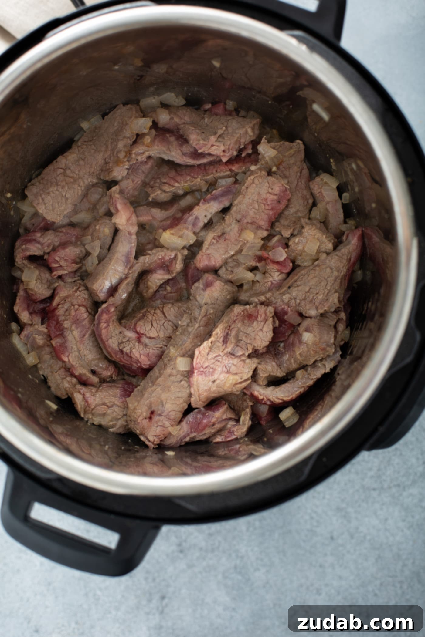 Instant Pot Beef and Broccoli A photo of sliced flank steak sauteeing in an Instant Pot.
