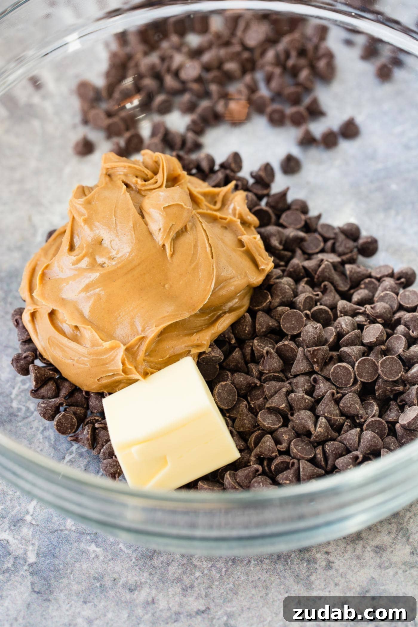 Chex Puppy Chow Muddy Buddies Mix A glass bowl full of chocolate chips, a large dollop of peanut butter and a chunk of unmelted butter.