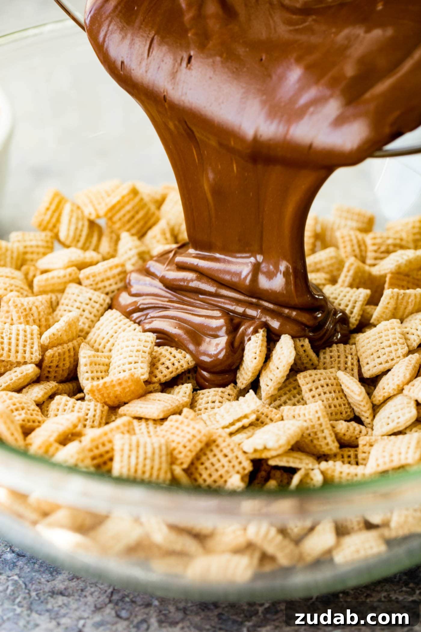 Chex Puppy Chow Muddy Buddies Mix Melted chocolate and peanut butter being poured over rice Chex in a glass bowl.