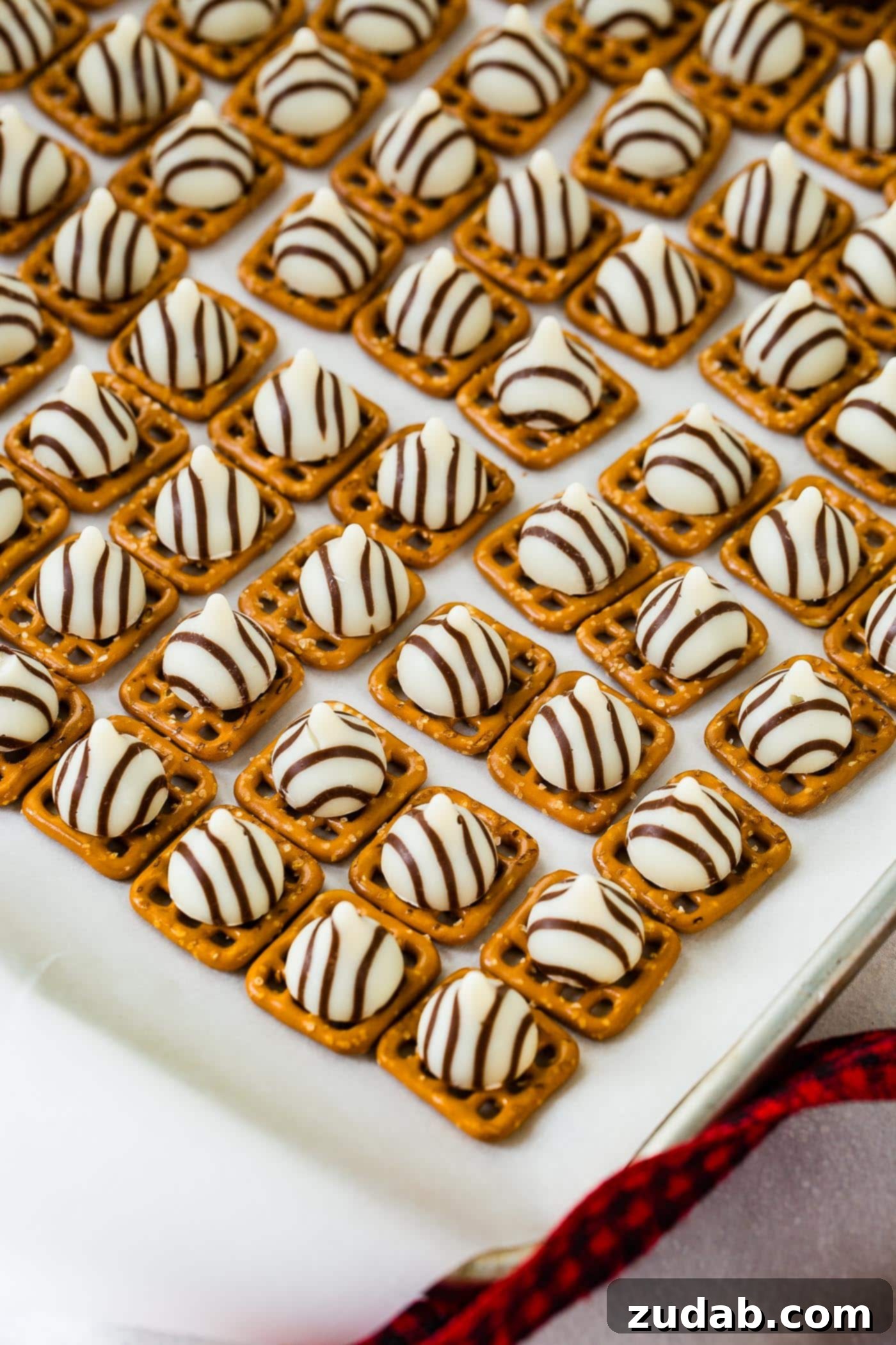 Addicting Christmas M&M Pretzel Hugs A cookie sheet lined with square pretzels, each topped with a Hershey's Hug chocolate