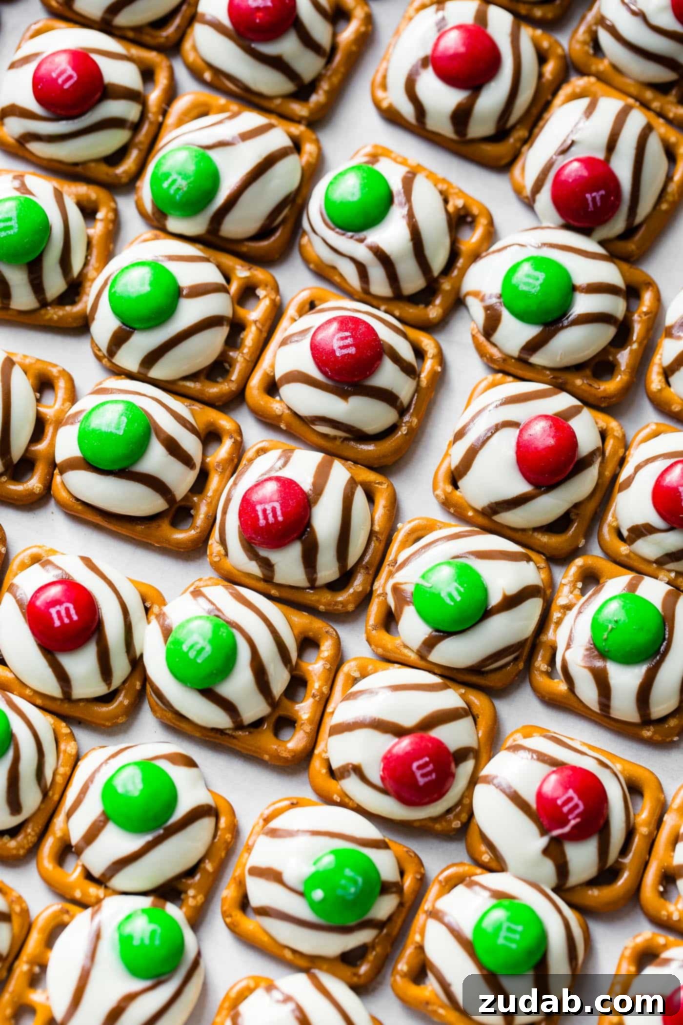 Addicting Christmas M&M Pretzel Hugs A cookie sheet filled with lines of completed Christmas M&M Pretzel Hugs