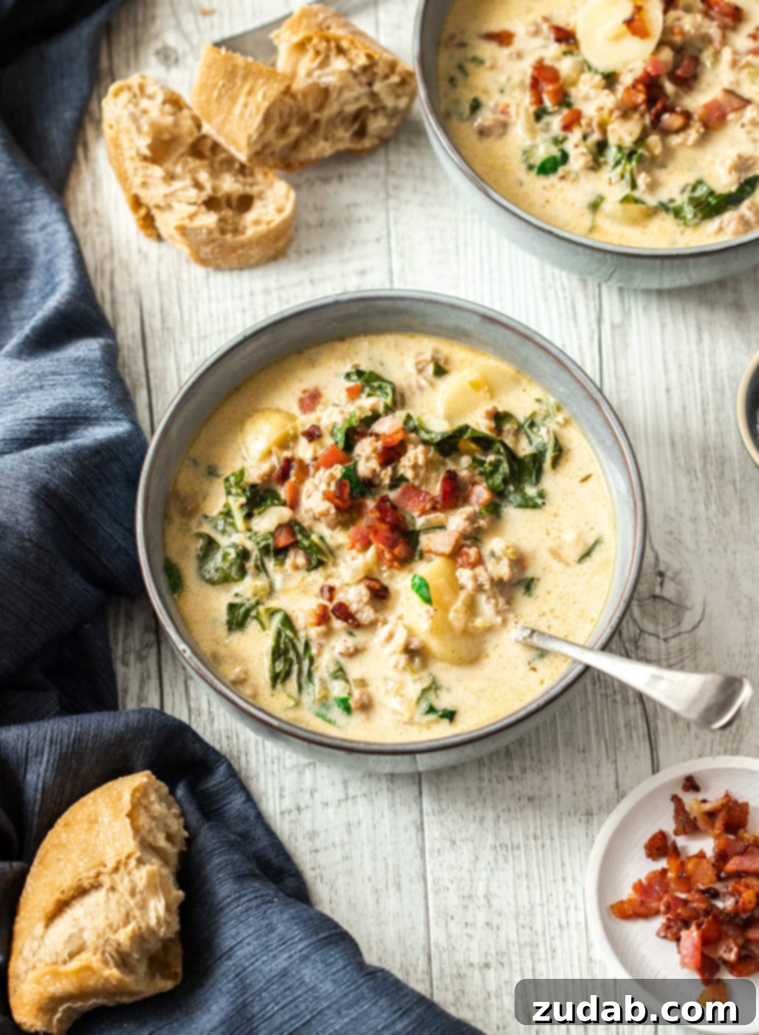 Creamy One Pot Zuppa Toscana 4 Bowls of zuppa toscana on a white timber table surrounded by chunks of bread