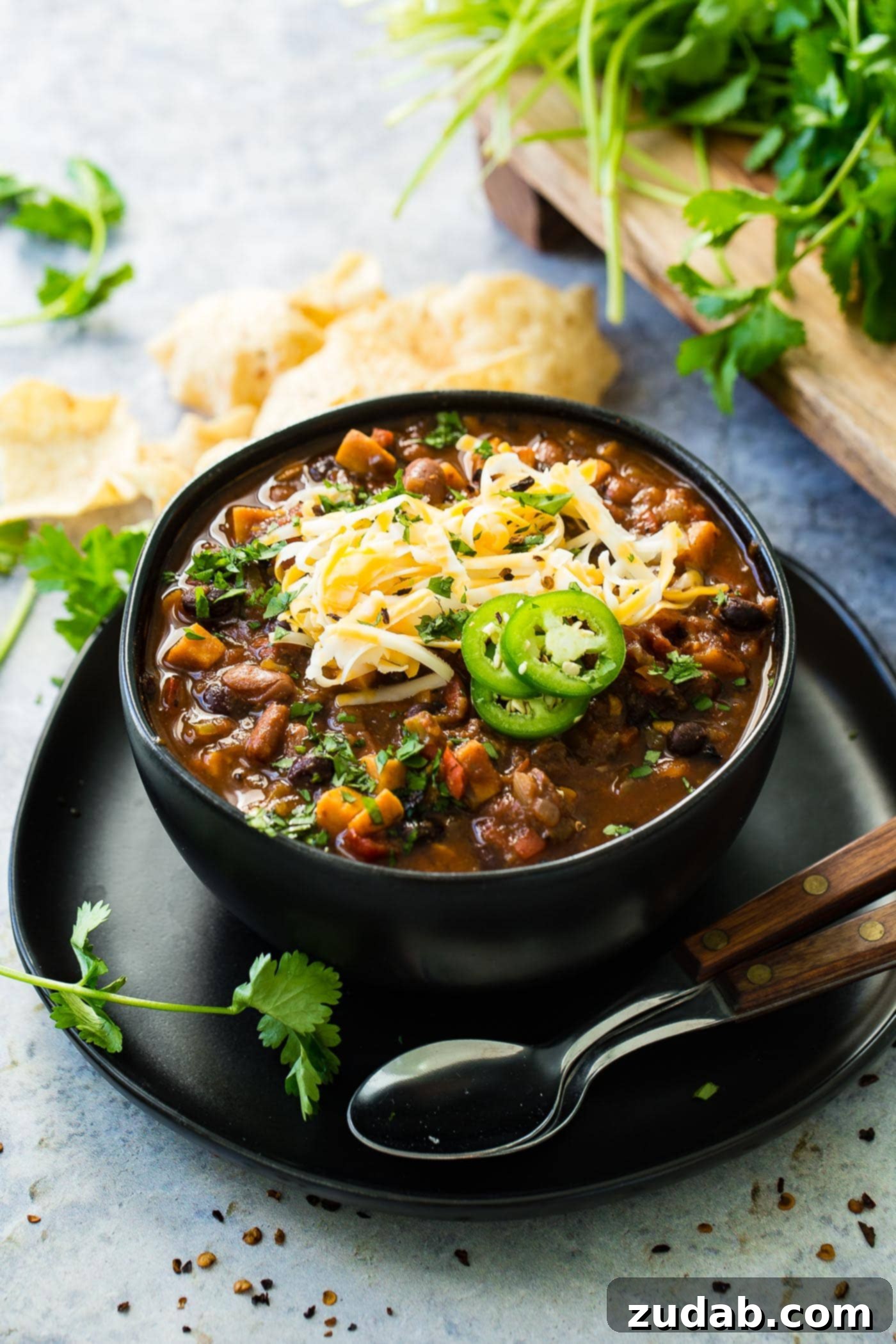 Instant Pot Vegetarian Chili A photo of a bowl of hearty meatless chili topped with shredded cheese and sliced jalapeno with two spoons sitting next to the bowl, ready to be enjoyed.