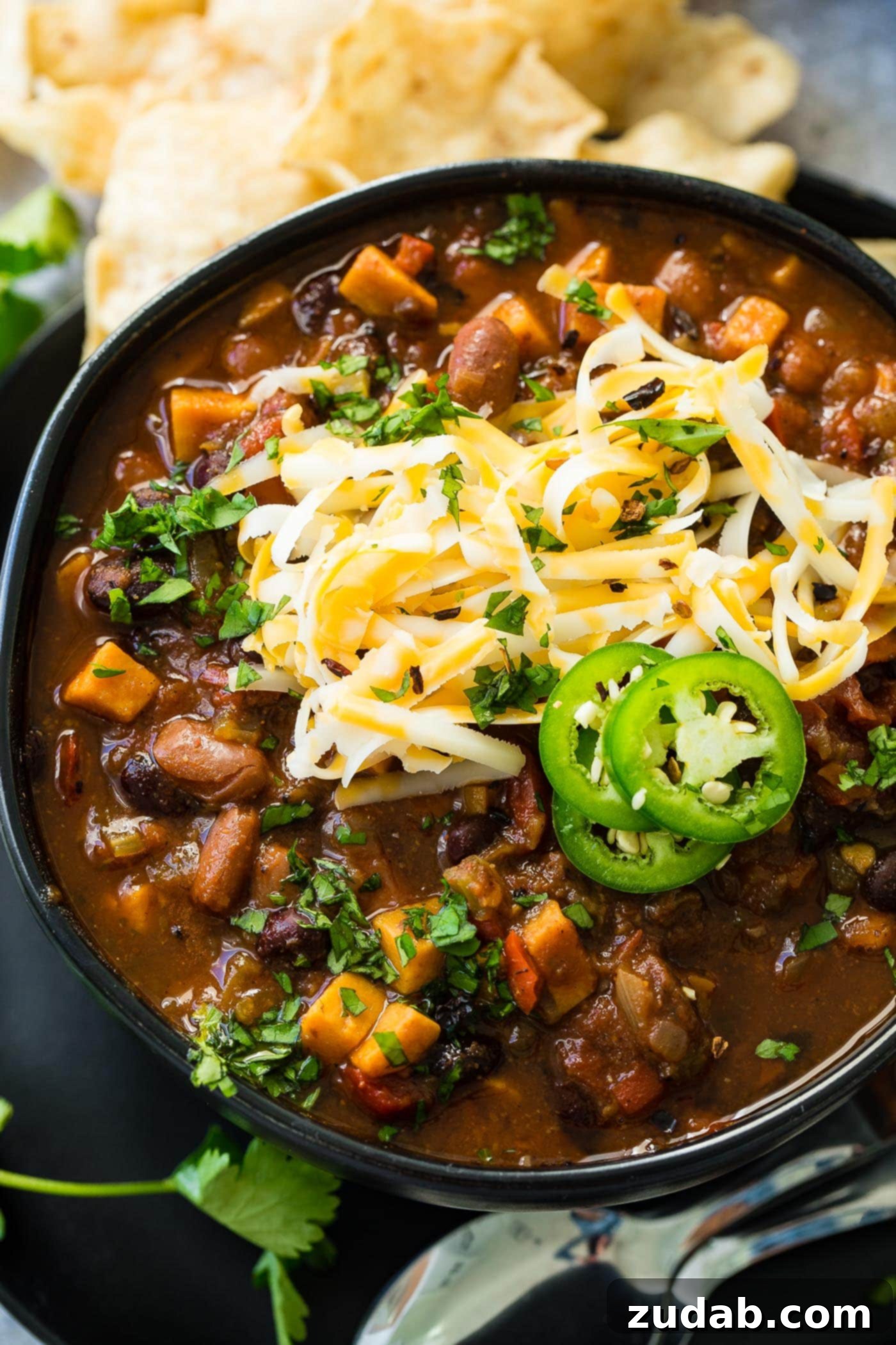Instant Pot Vegetarian Chili A photo of a bowl of instant pot veggie chili, steaming and vibrant, topped generously with shredded cheese and fresh jalapeno slices.