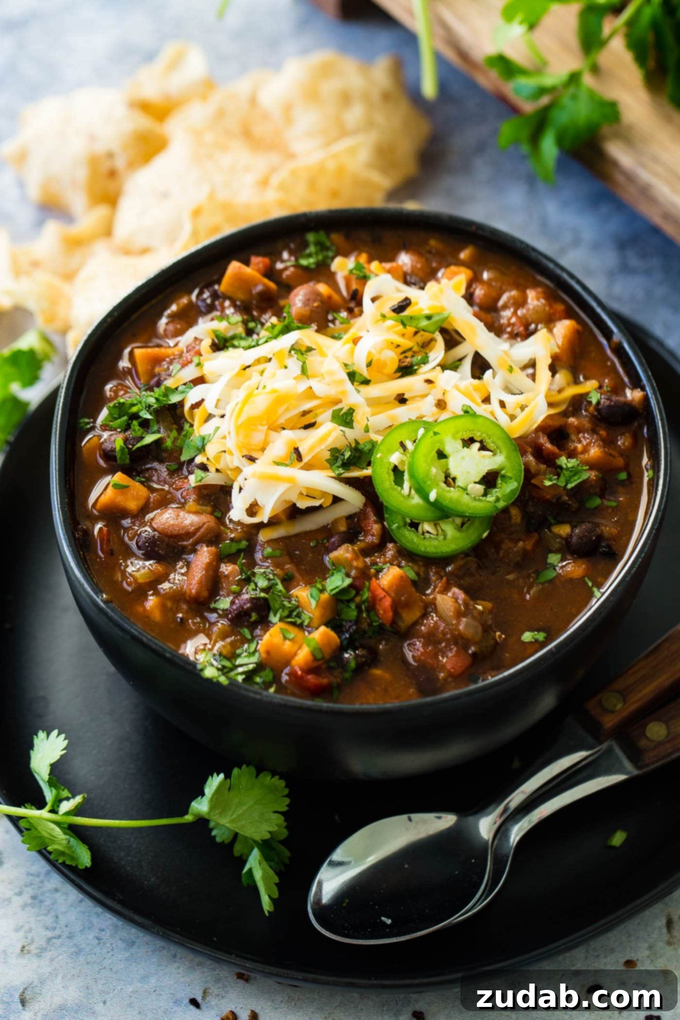Instant Pot Vegetarian Chili A close-up photo of a bowl of hearty veggie chili topped with shredded cheese and sliced jalapeno with two spoons sitting next to the bowl, illustrating its rich texture.