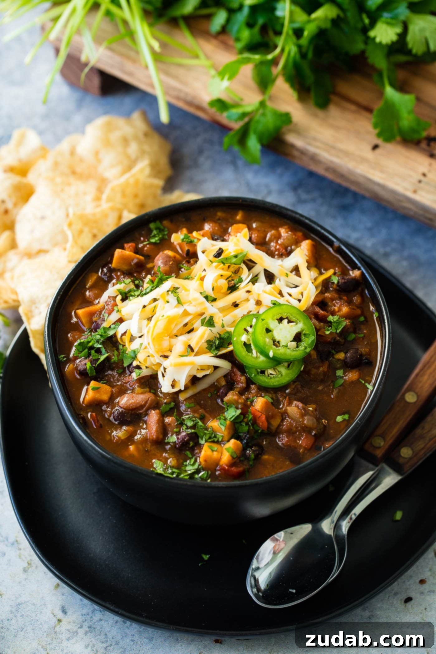 Instant Pot Vegetarian Chili A close-up photo of a bowl of Instant Pot meatless chili, thick and rich, topped with melted shredded cheese and bright green sliced jalapeno, with two spoons.