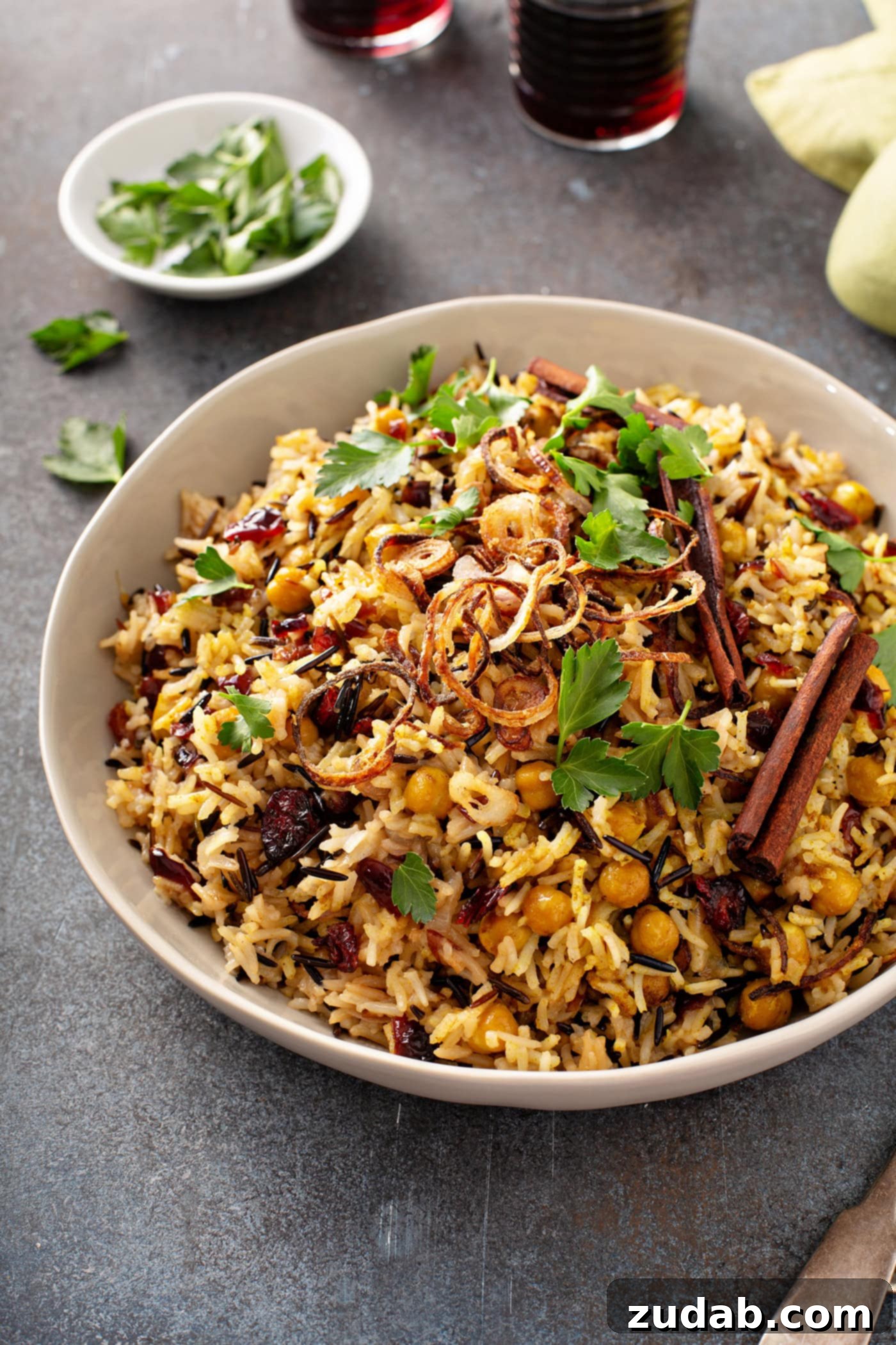 Wild Rice and Chickpeas with Crispy Shallots A photo of a large serving bowl of Jerusalem wild rice topped with fried shallots, spiced chickpeas, chopped fresh parsley and cinnamon sticks.