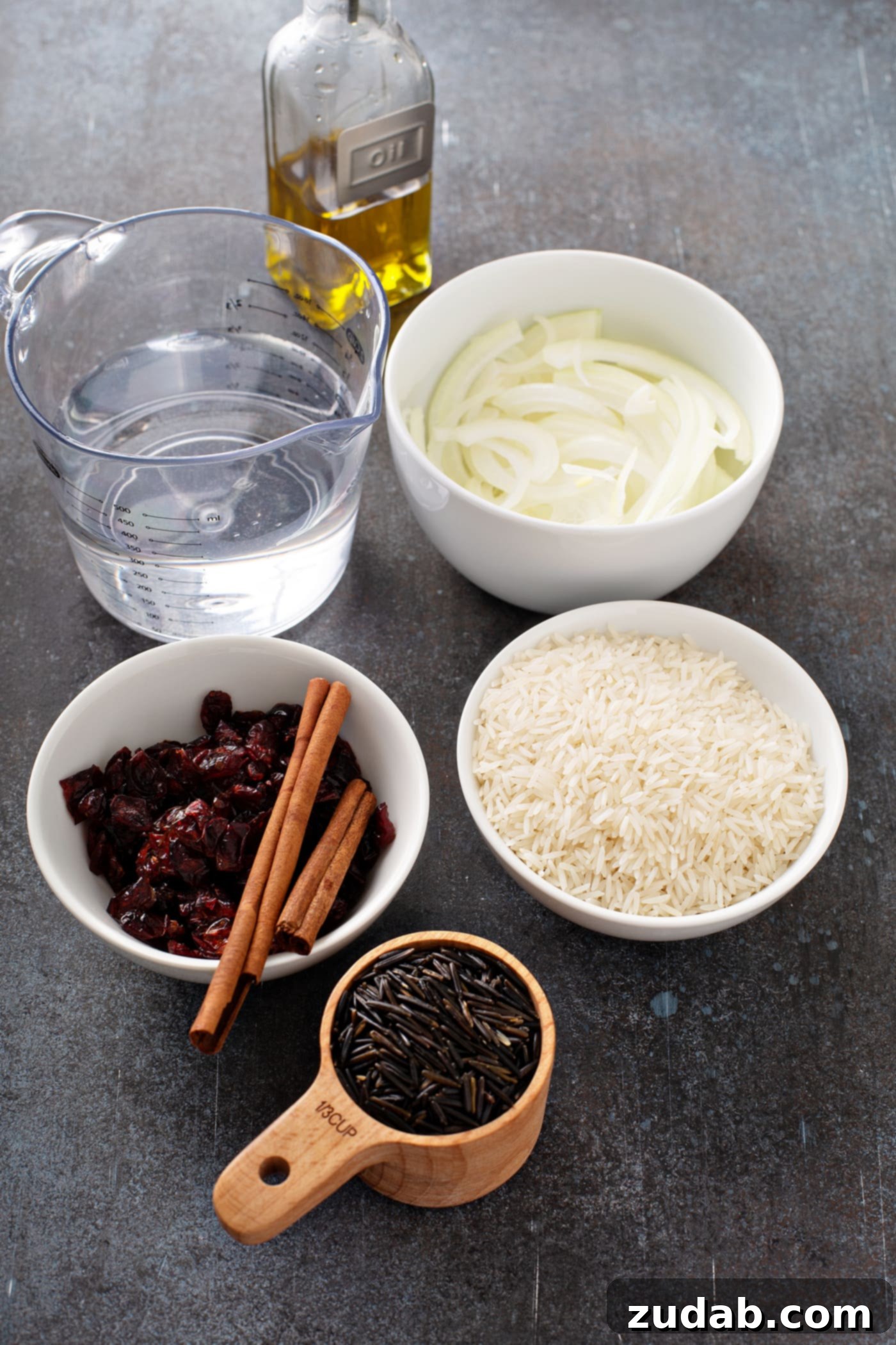 Wild Rice and Chickpeas with Crispy Shallots A photo of all the ingredients for Jerusalem wild rice in separate bowls including water, olive oil, sliced onions, basmati rice, craisins, cinnamon sticks and wild rice.