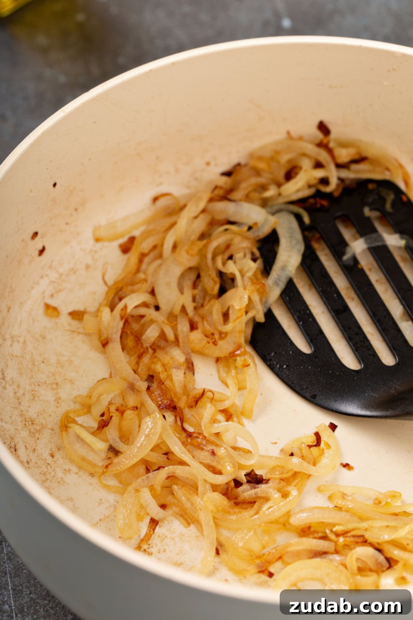 Wild Rice and Chickpeas with Crispy Shallots A photo of sliced shallots being fried in a pan with a spatula stirring them.