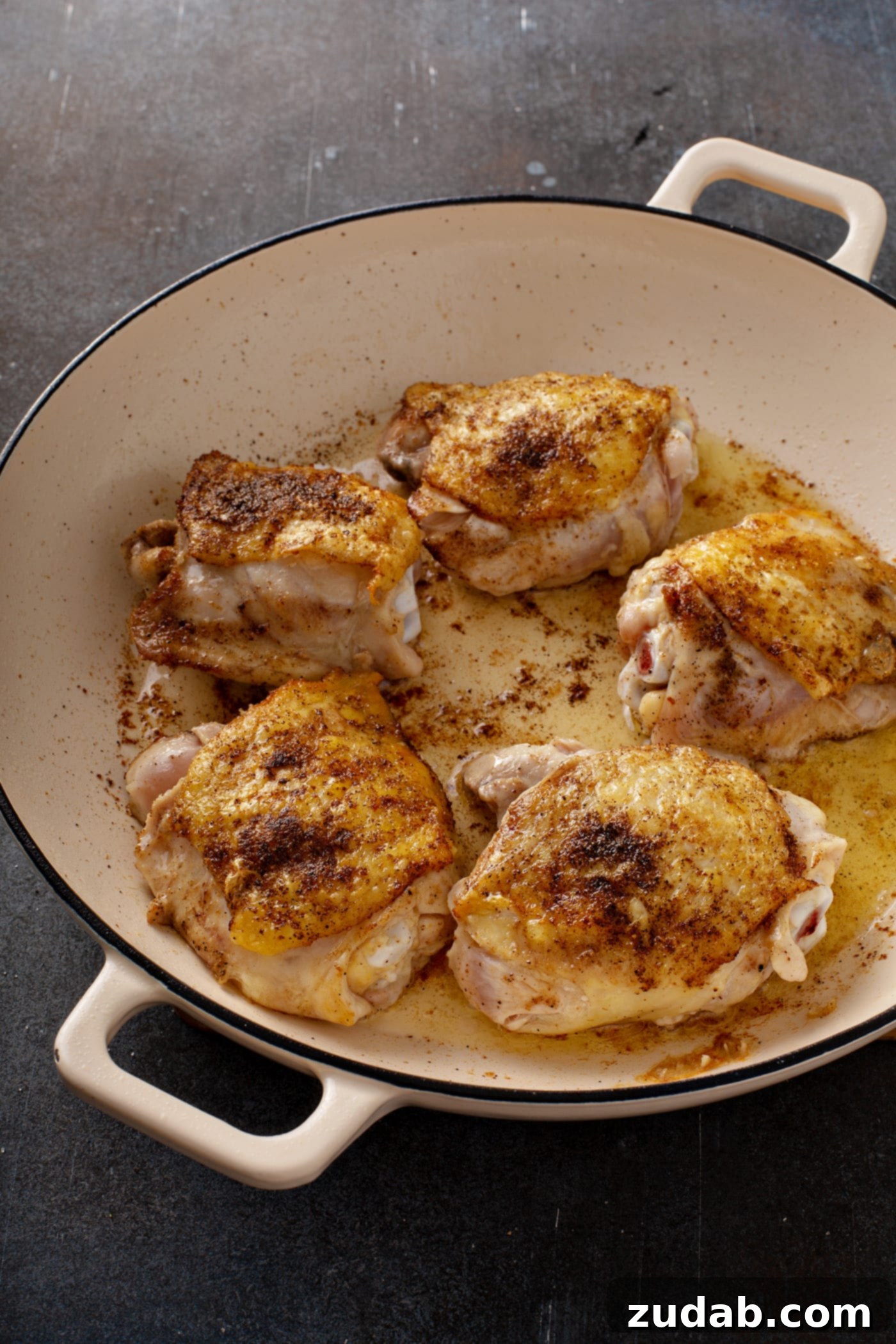 Golden Brown Chicken Thighs Sizzling in a Skillet A vibrant photo of five bone-in chicken thighs, cooking to a golden crisp in a hot skillet, with their skin perfectly browned and sizzling.