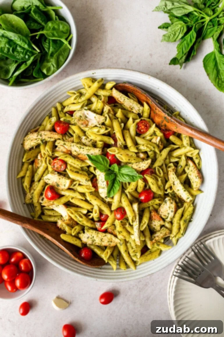 Lemon Basil Chicken Pasta 8 a photo of a large bowl of penne pasta tossed in a bright green sauce with cherry tomatoes, chicken strips and wooden serving spoons in the bowl