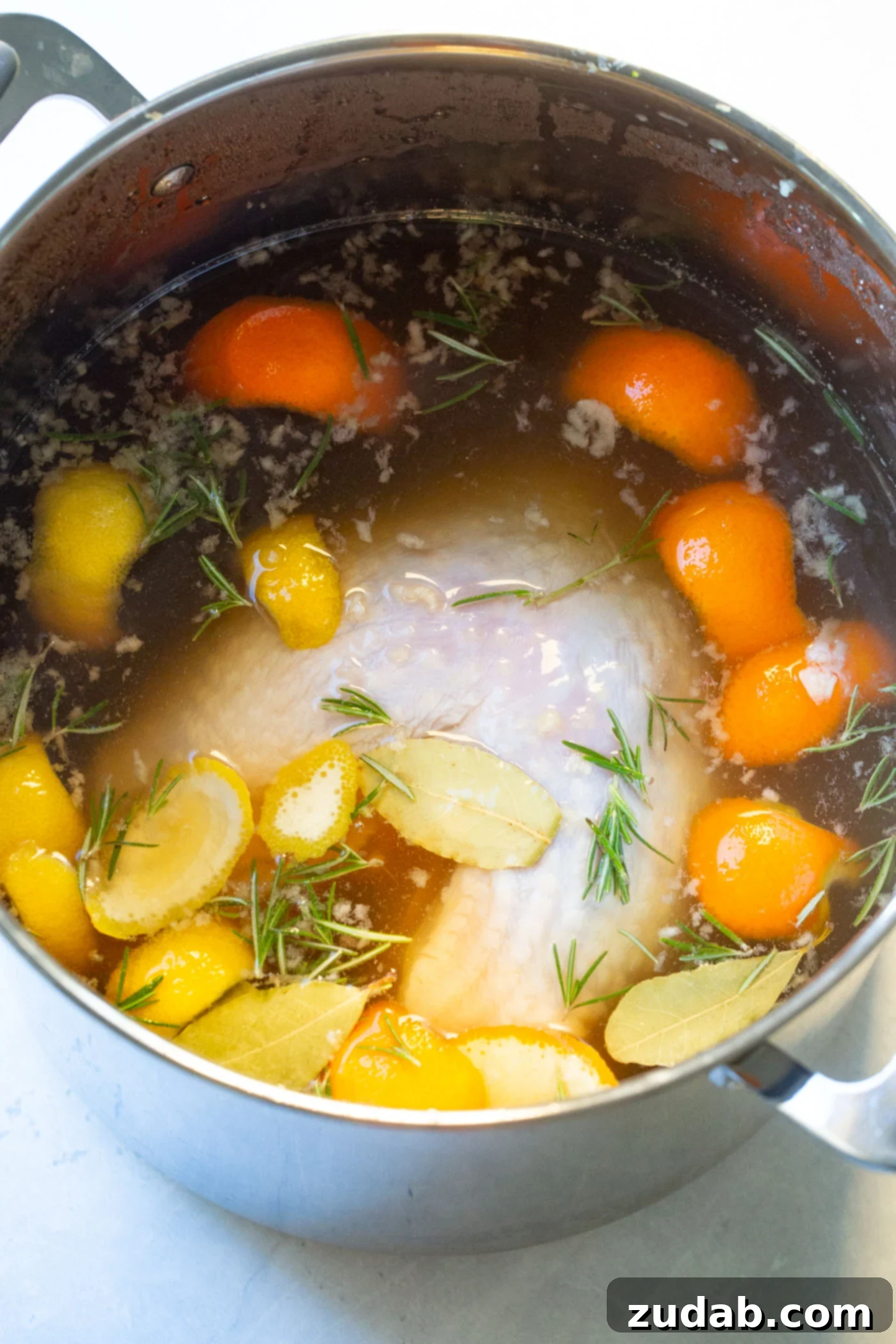 A photo of turkey brine in a large stock pot with fresh herbs, orange and lemon peels. 
