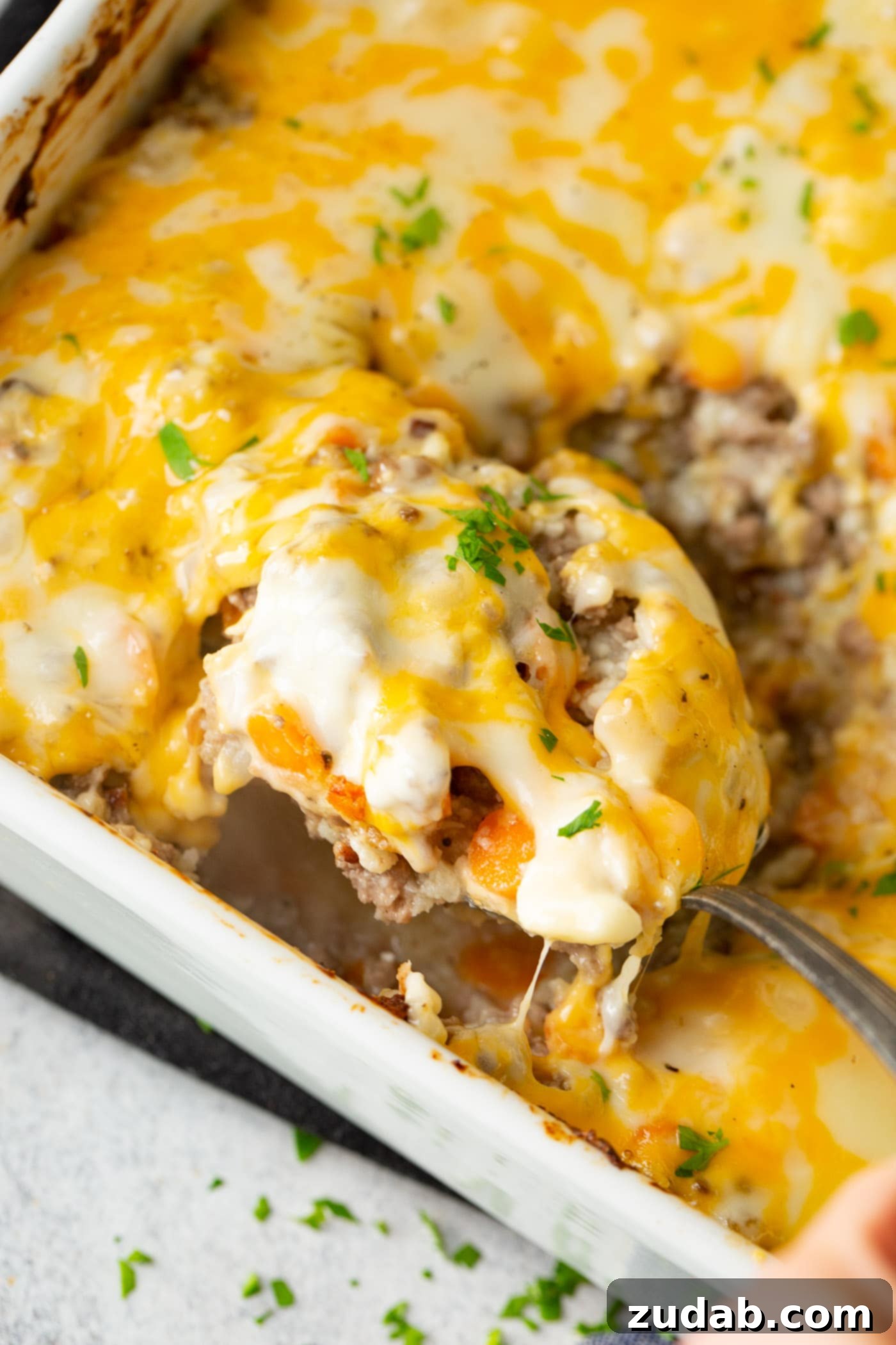 Low Carb Cheesy Ground Beef and Cauliflower Rice Casserole A photo of a baking dish full of low carb cheesy ground been and cauliflower rice casserole with a spoon taking a scoop out.
