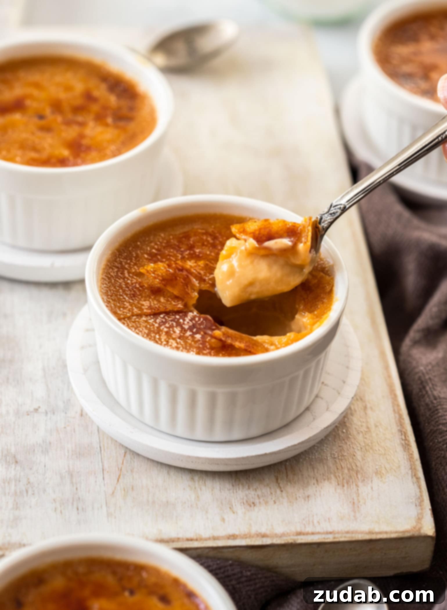 A spoon coming out of a rich, creamy salted caramel crème brûlée with a perfectly torched sugar crust, resting on a clean white surface.