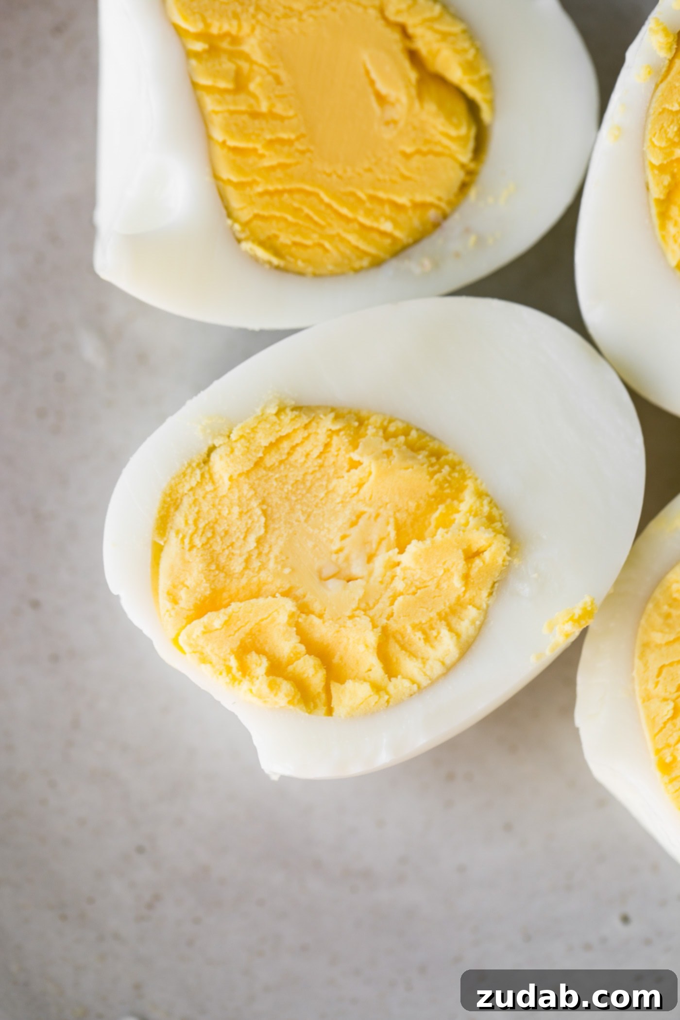 How to Make Perfect Hard Boiled Eggs Two perfectly cooked hard boiled eggs, sliced in half to reveal bright yellow yolks.